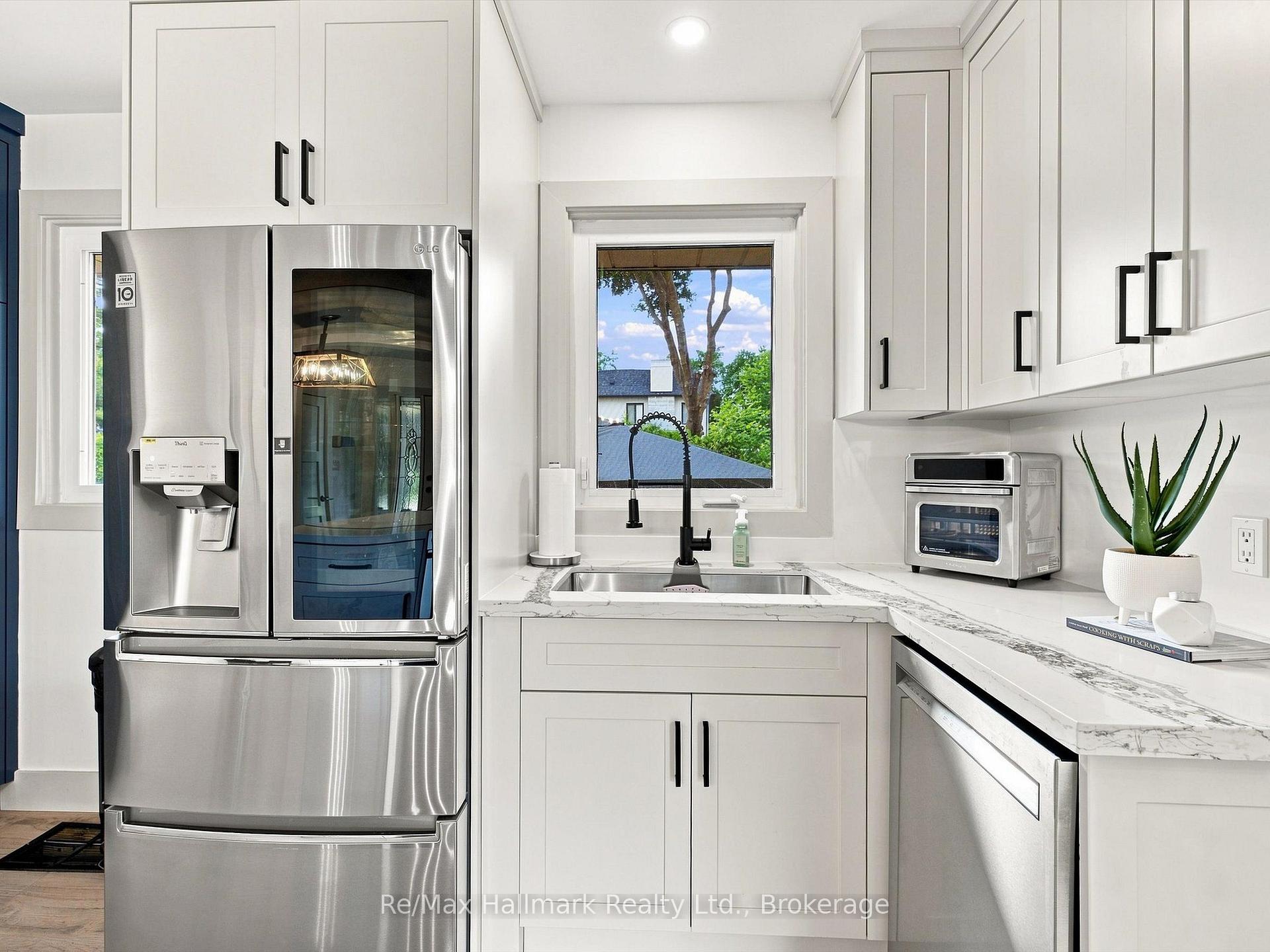 Bright white kitchen with stainless steel refrigerator, marble-patterned counters, and a window above the sink.