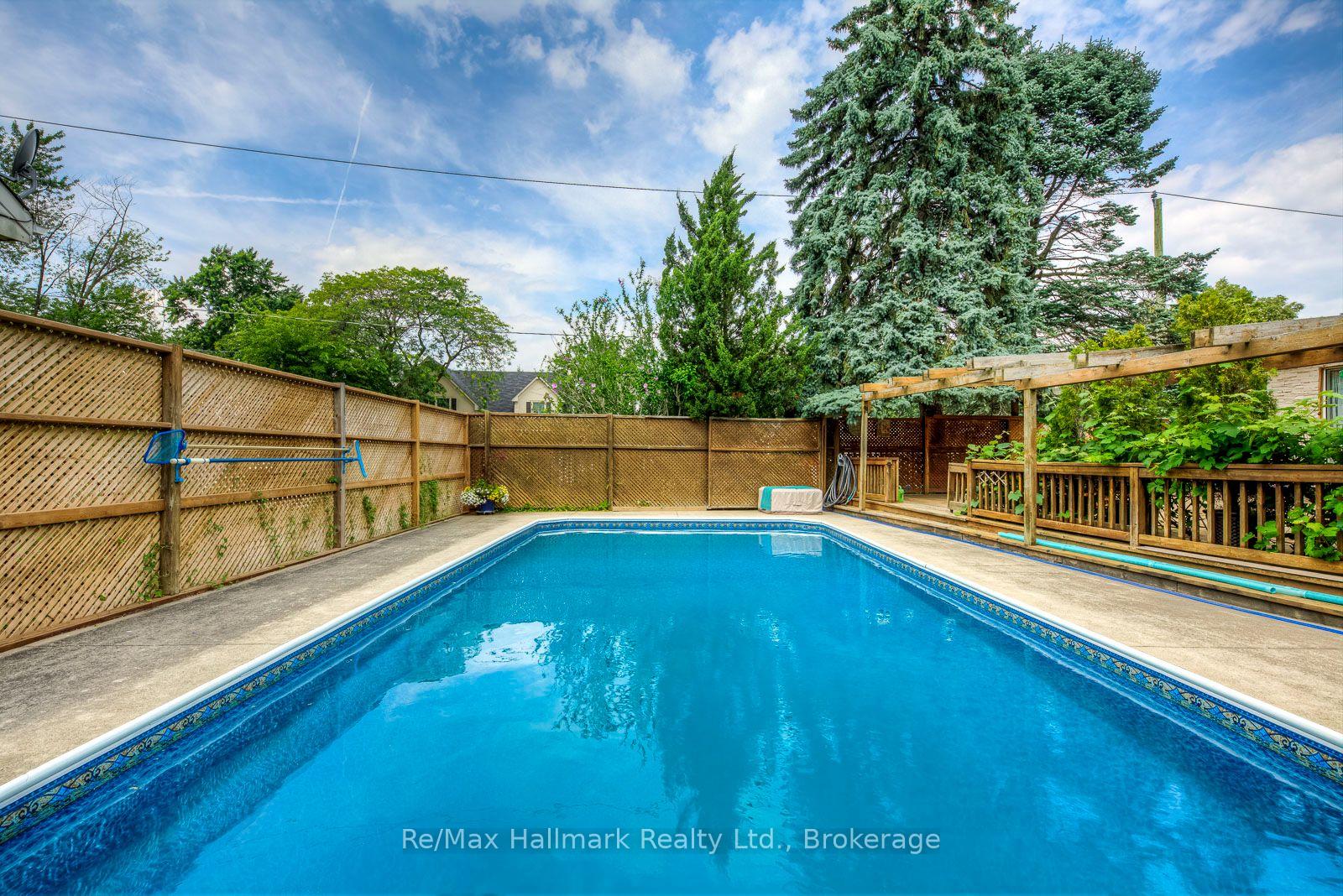 Backyard swimming pool bordered by lattice fencing, mature trees, and a wooden pergola.