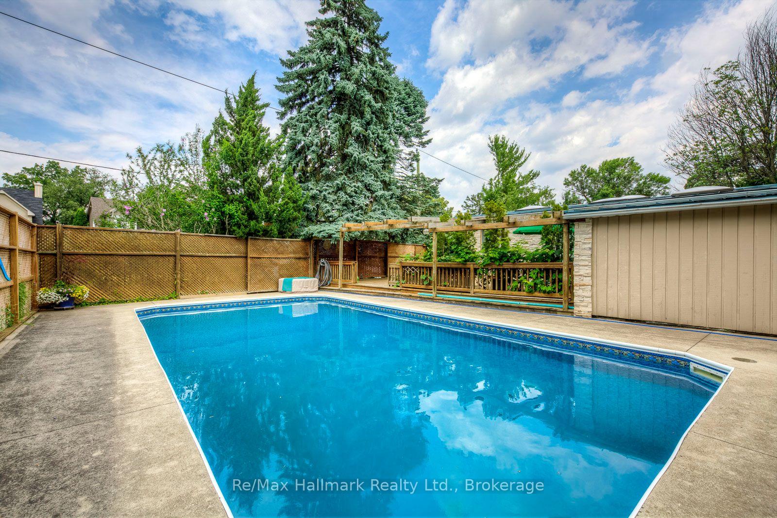 Backyard swimming pool surrounded by a concrete deck, wooden fencing, and mature trees.