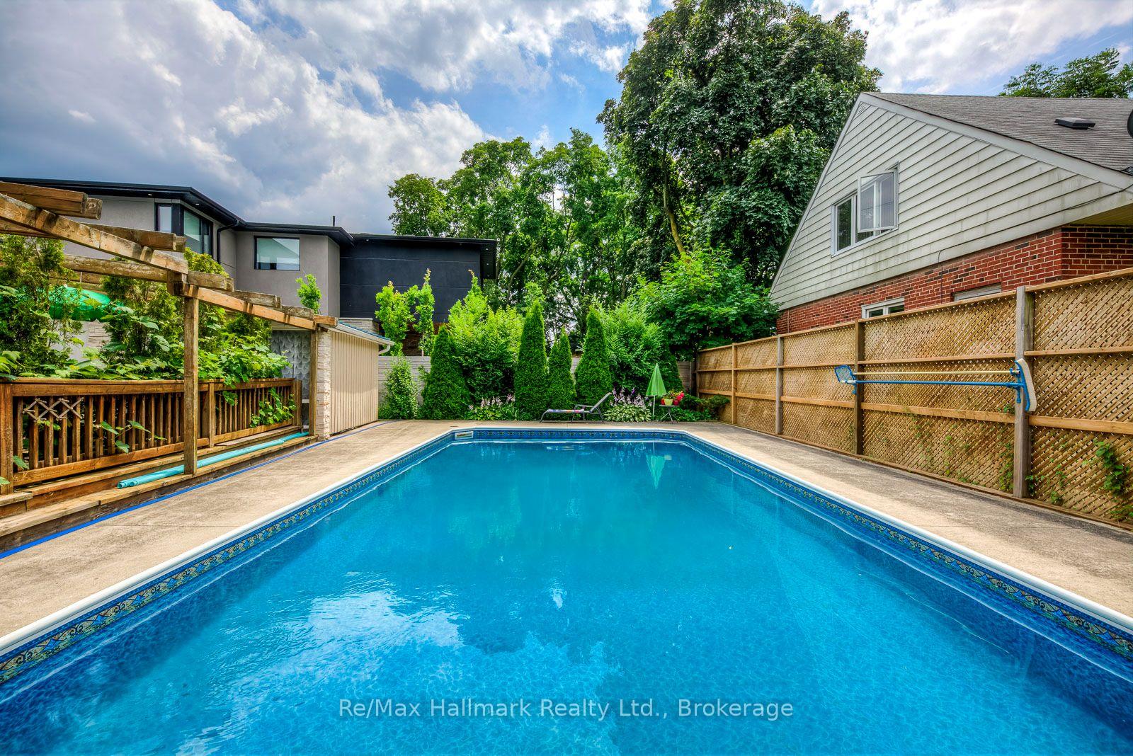 Backyard swimming pool beside a modern home, with a wooden pergola and privacy fencing.