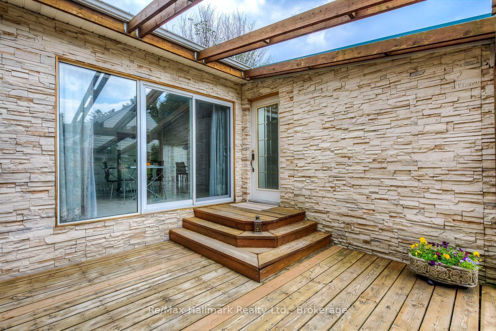 Covered wooden deck with stone walls, a glass door, and a small flower planter.