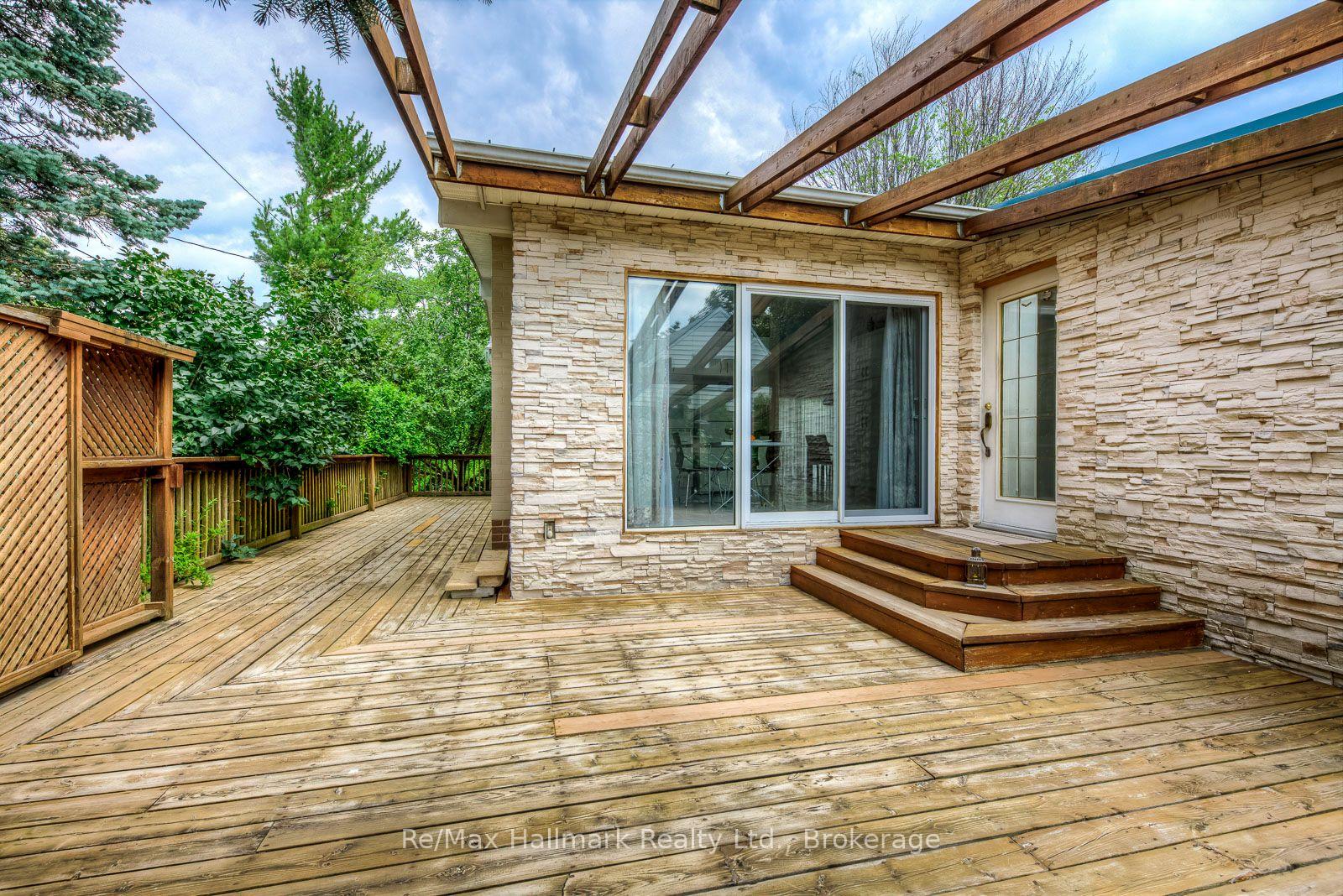 Wooden backyard deck beneath open pergola beams, beside a stone-clad house.