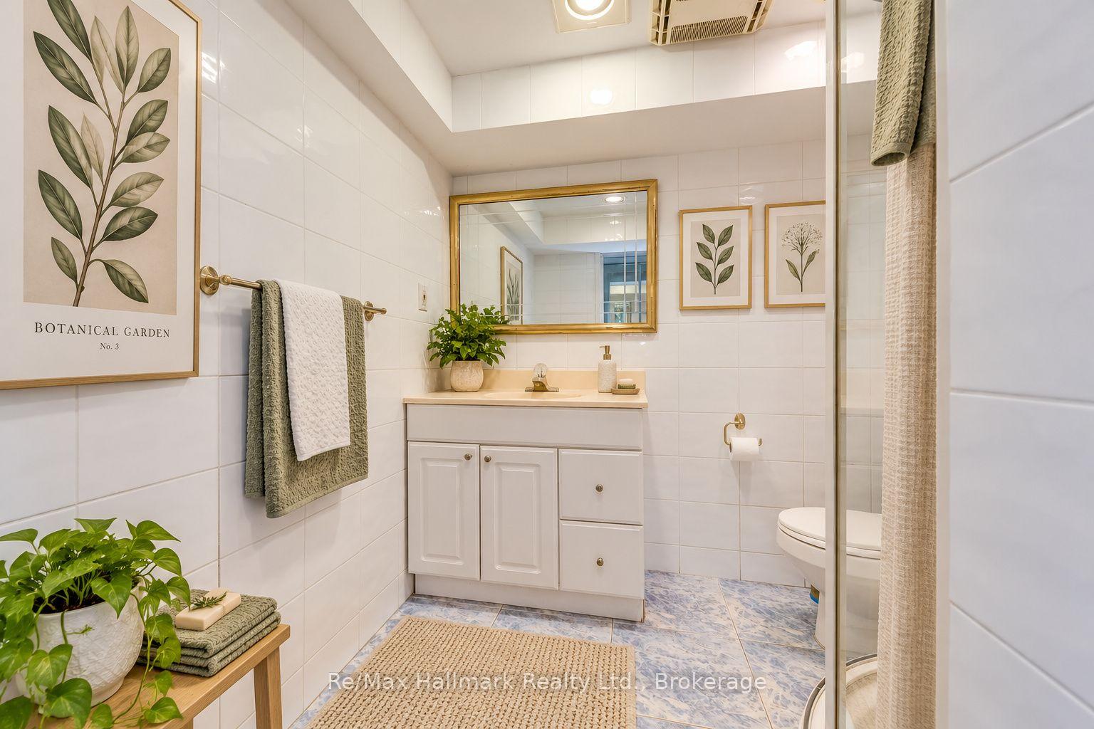 Bathroom with white tile, a gold-framed mirror, botanical prints, and a glass shower enclosure.
