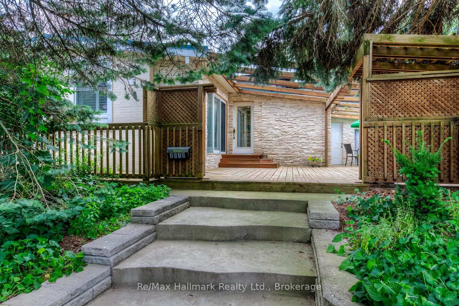 Home entrance with stone facade, wooden deck, and tree-shaded steps.