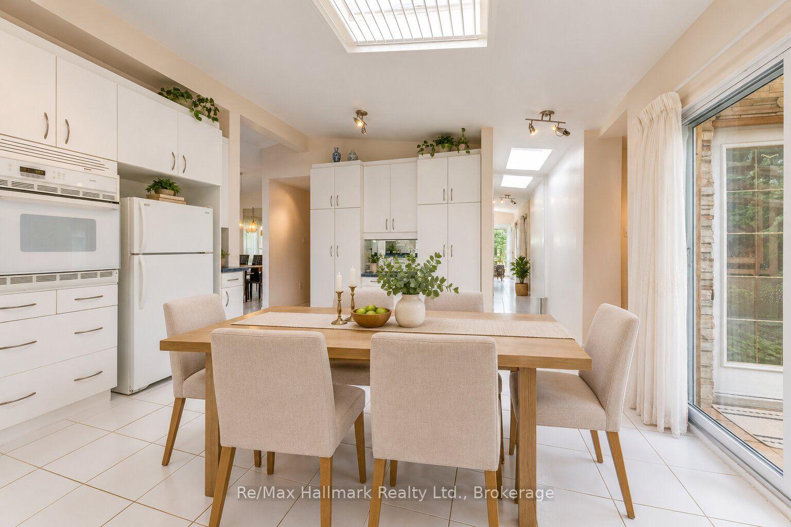 Bright kitchen and dining area with white cabinetry, skylights, and a table beside sliding glass doors.