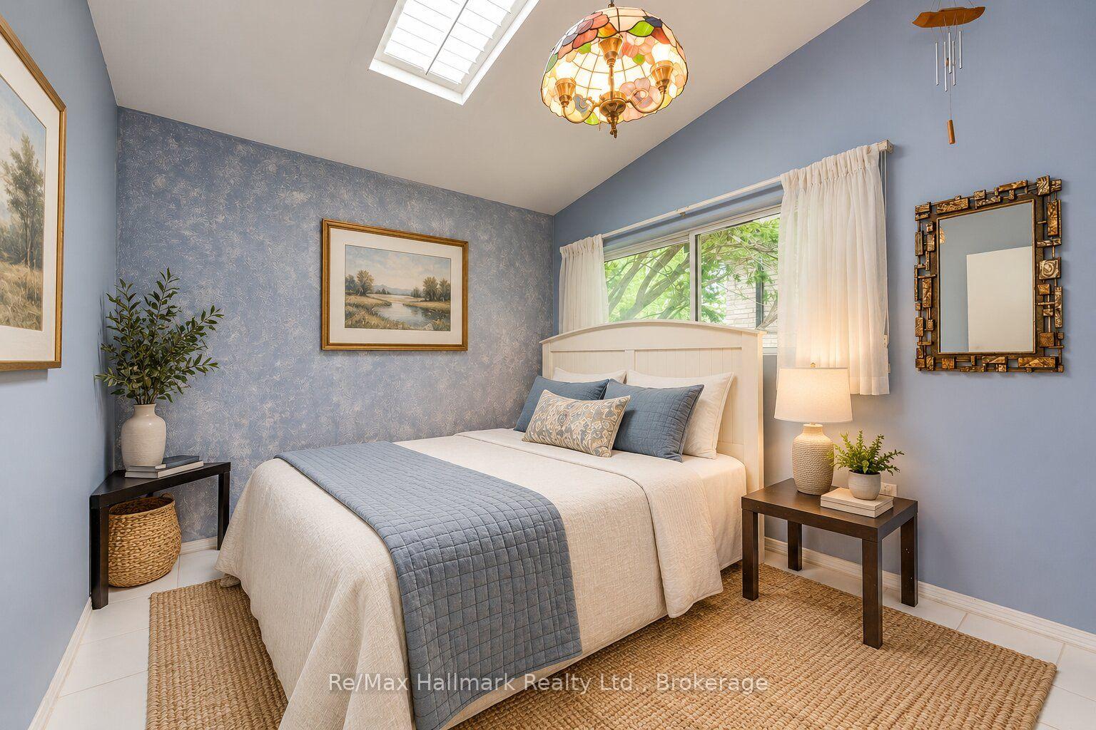 Staged bedroom with a white bed, blue walls, skylight, and stained-glass pendant light.