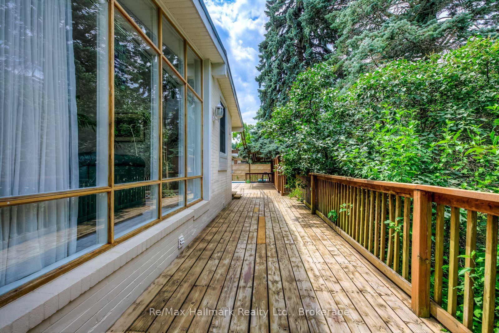 Wooden deck beside a home, with broad windows and a leafy privacy hedge.