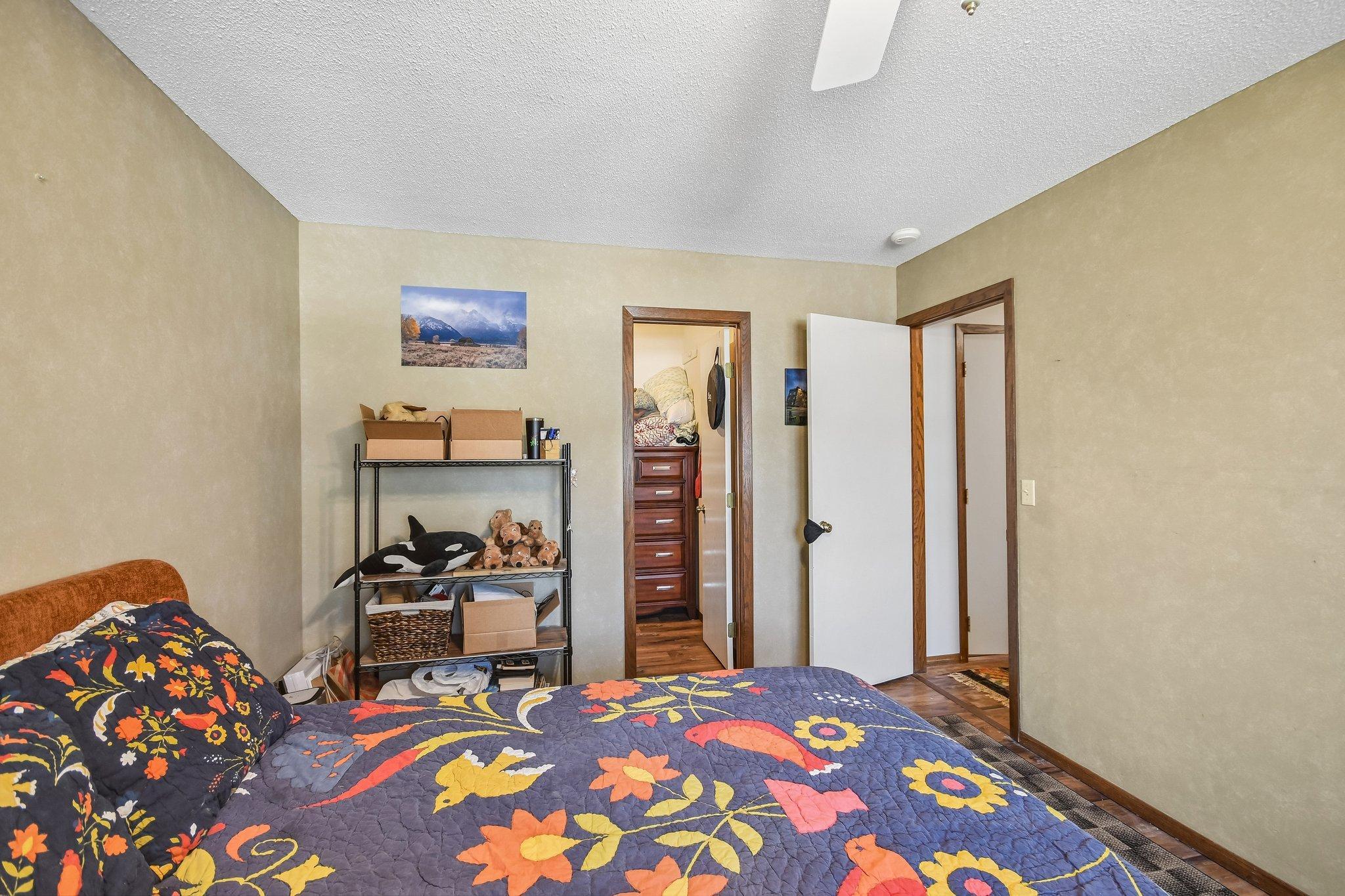 Bedroom with a bright floral quilt and storage shelving beside open doorways.