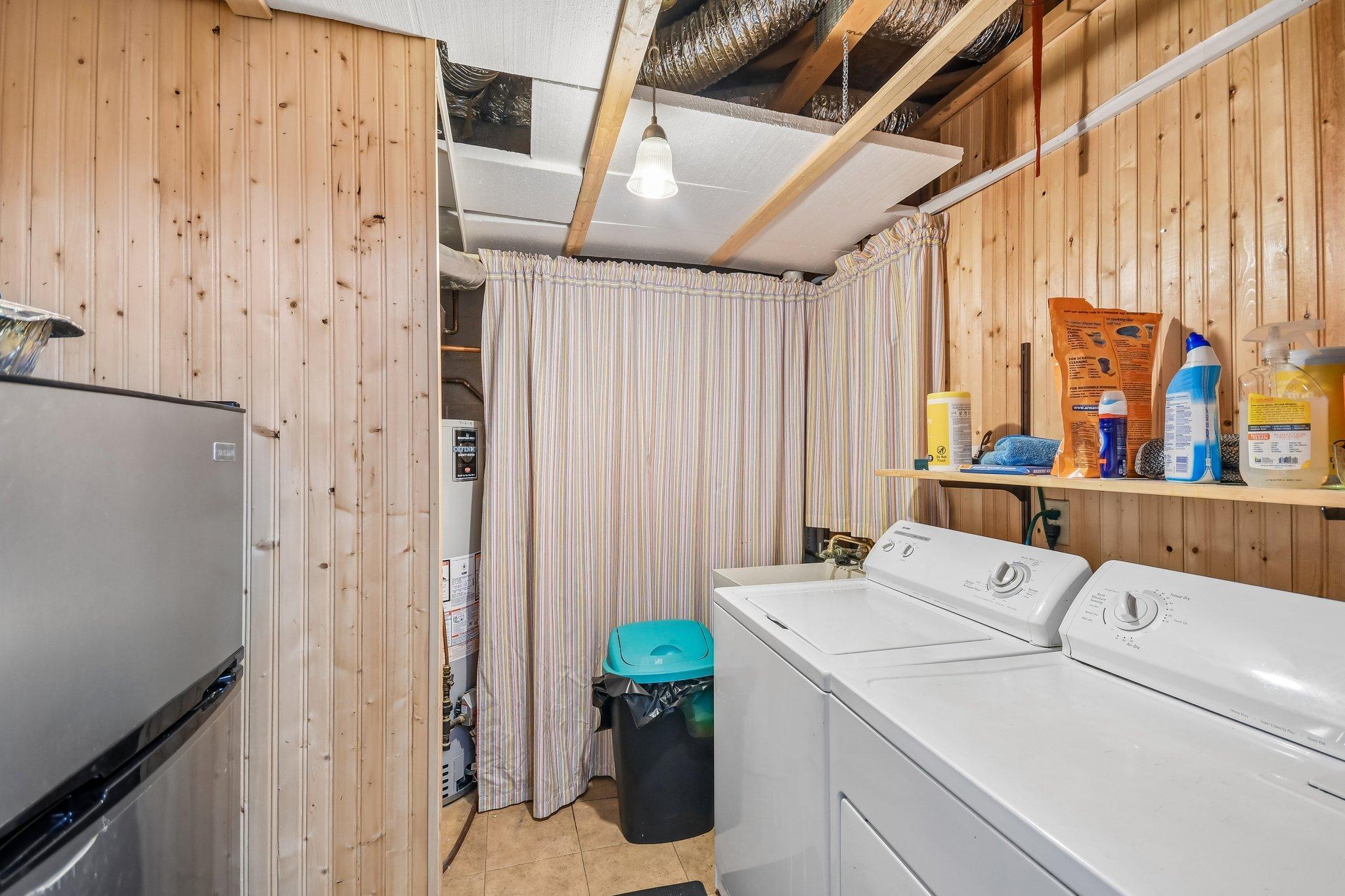 Laundry room with white washer and dryer, wood-paneled walls, and a striped curtain over utility equipment.