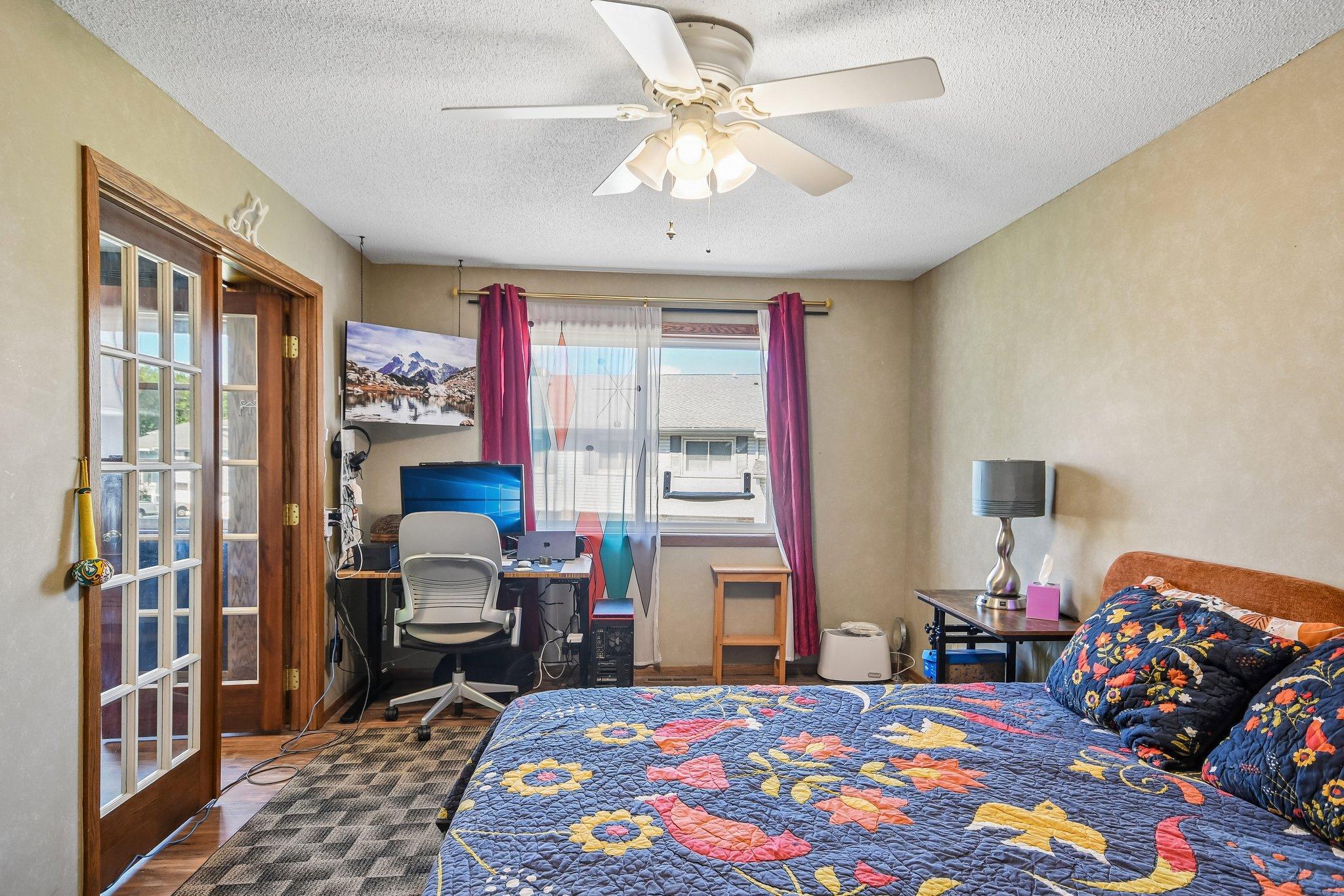 Bedroom with a colorful floral quilt and a computer desk beside the window.