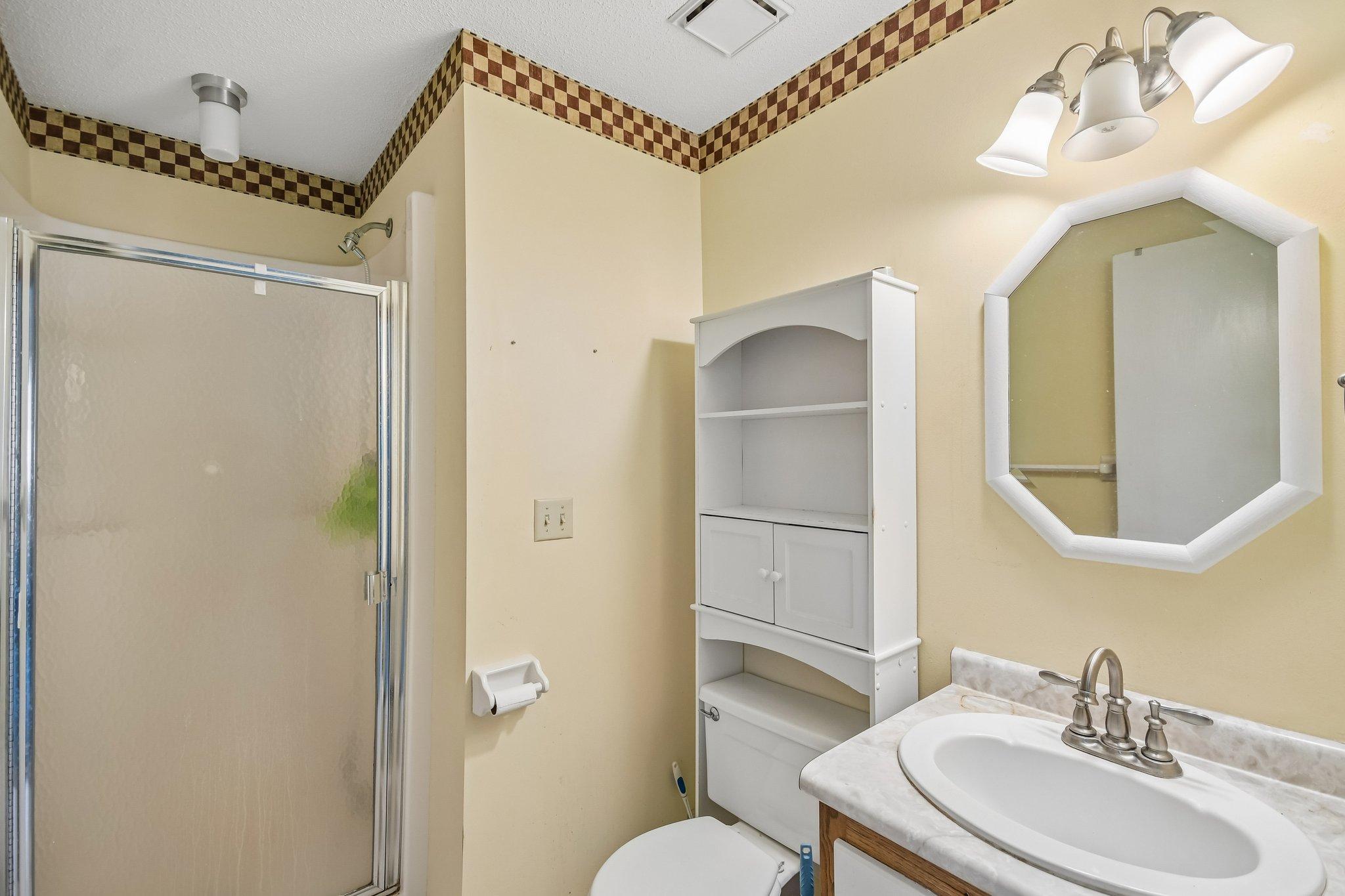 Bathroom with glass shower, octagonal mirror, white storage cabinet, and checkered tile border.