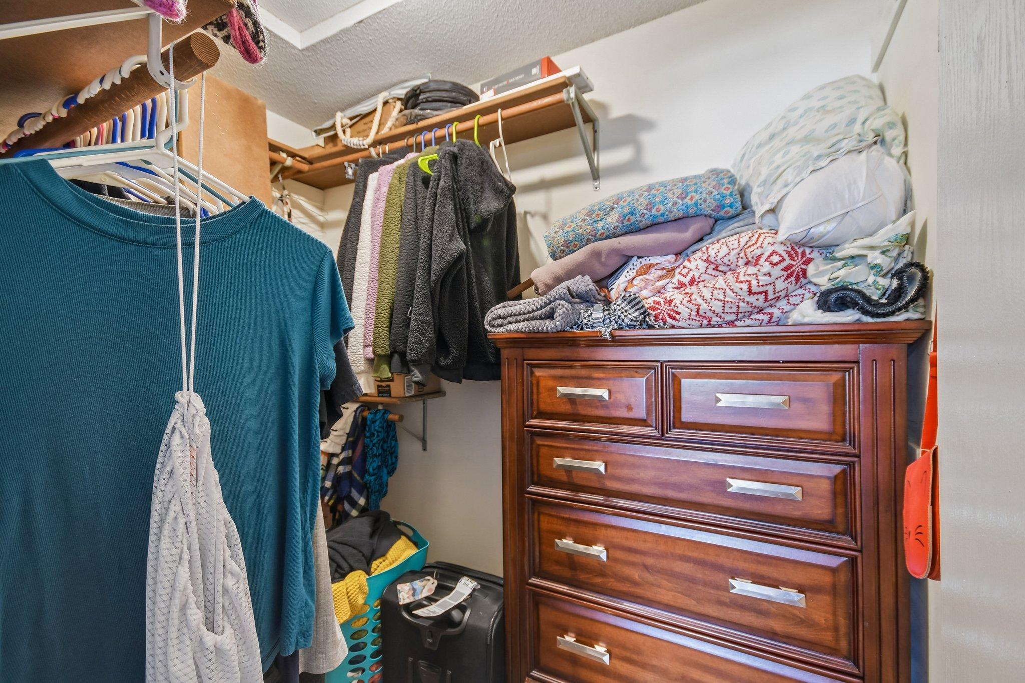 Walk-in closet with hanging clothes, stacked linens, and a large wooden dresser.