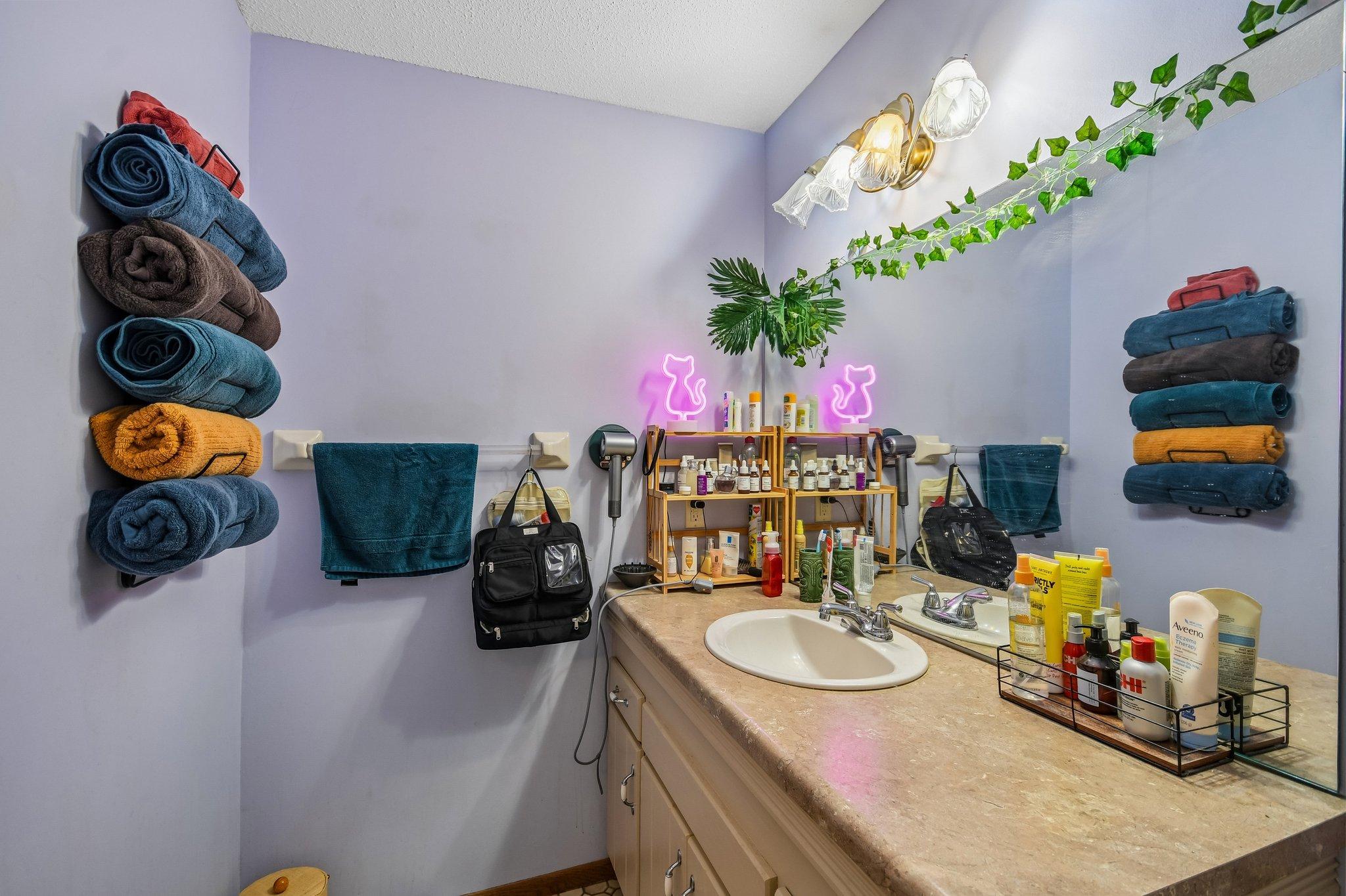 Bathroom vanity with an oval sink, colorful towels, toiletries, and pink cat-shaped lights.