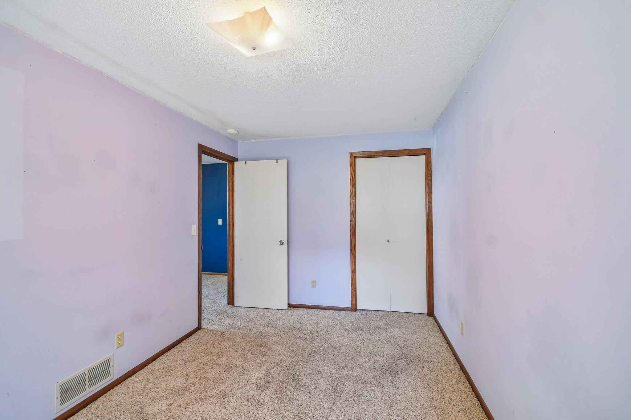 Empty bedroom with lavender walls, beige carpet, and a double-door closet.