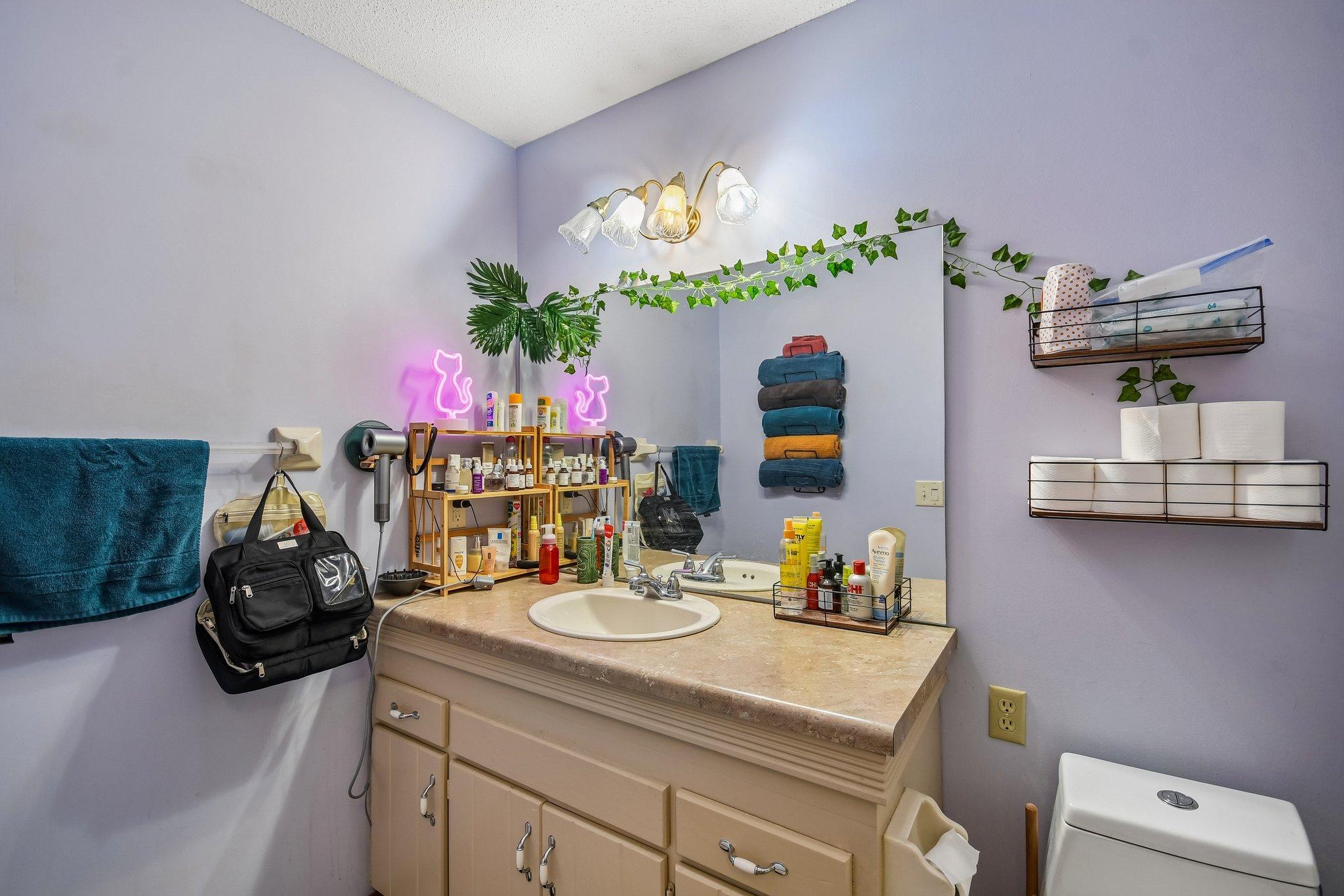 Bathroom vanity with oval sink and large mirror, surrounded by shelves of towels and toiletries.
