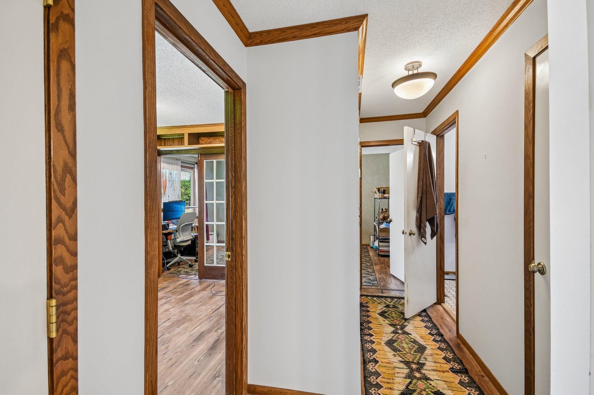 Hallway with dark wood trim and a patterned runner, opening onto an office and adjacent rooms.