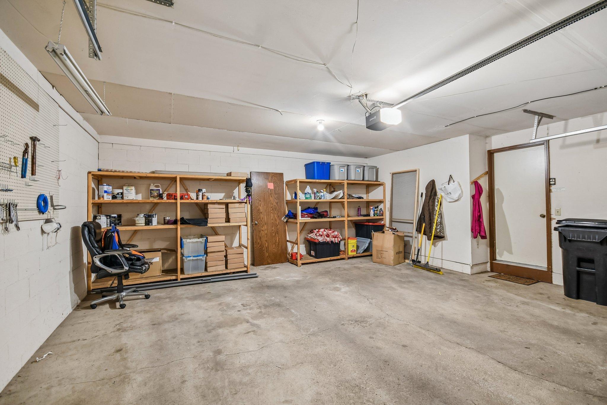 Garage with stocked wooden shelves, a tool pegboard, and a wide concrete floor.