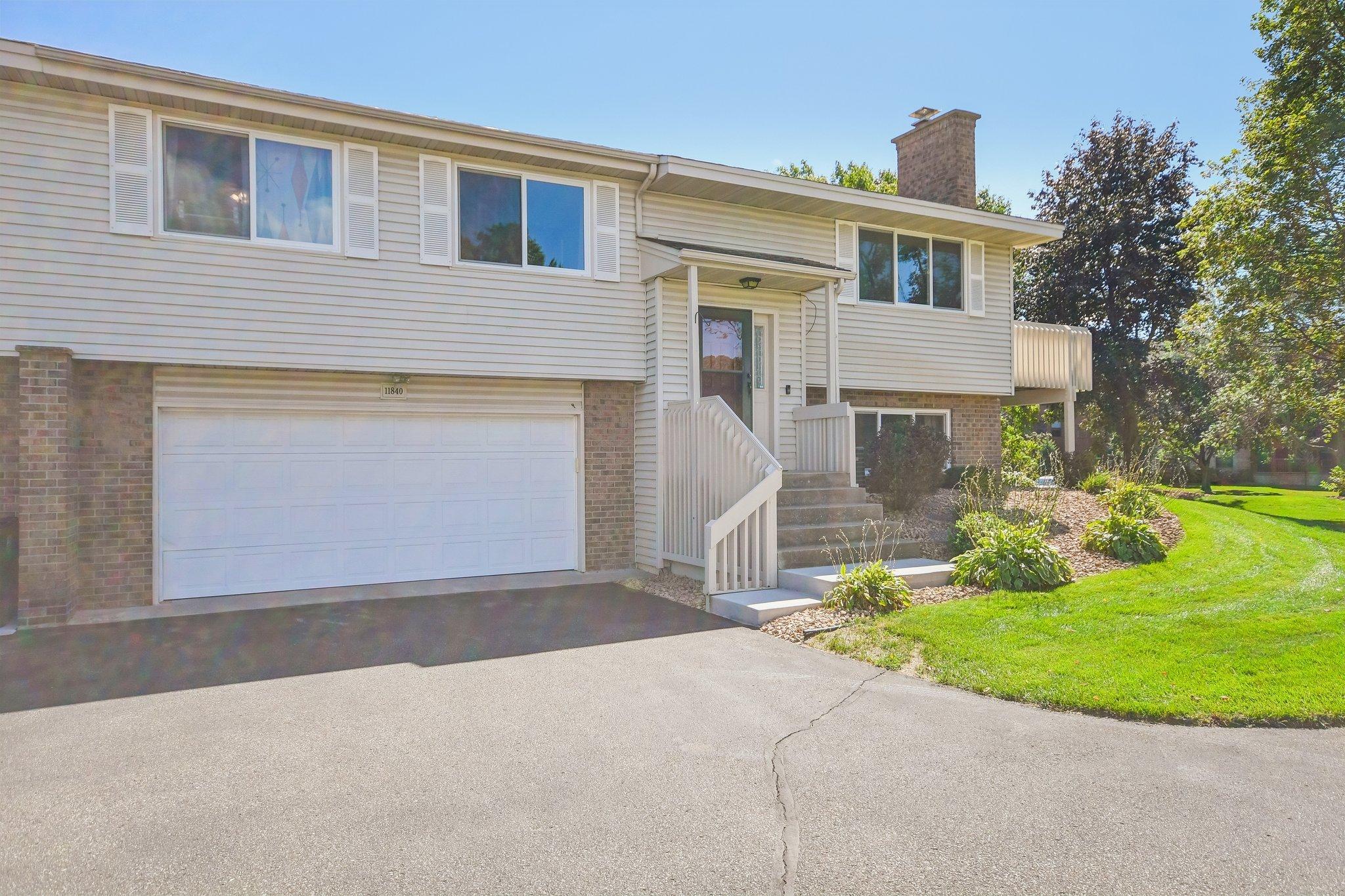Split-level home with light siding, brick accents, a two-car garage, and landscaped front yard.