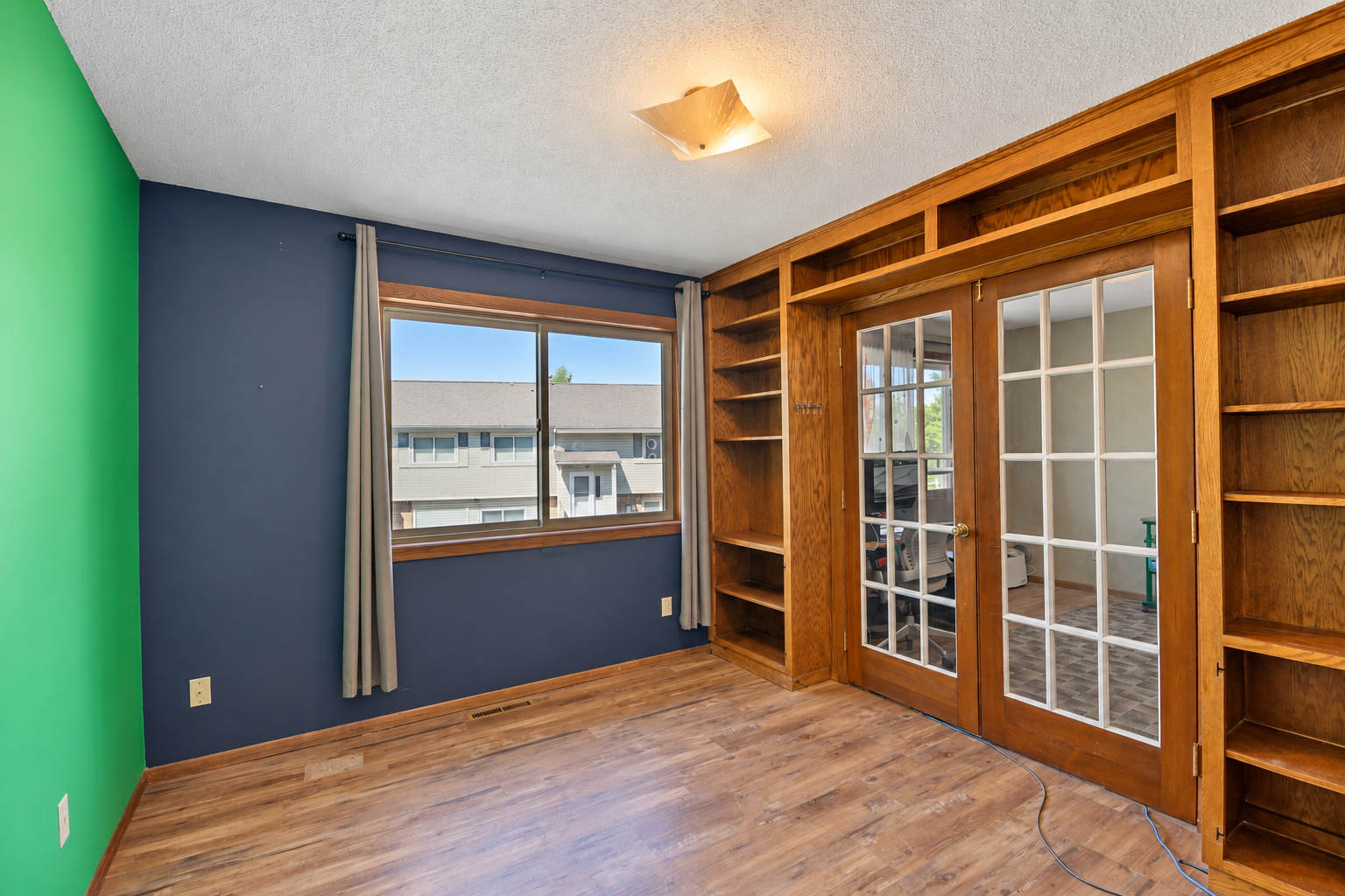Vacant room with built-in wooden shelves, glass-paneled French doors, and wood-look flooring.
