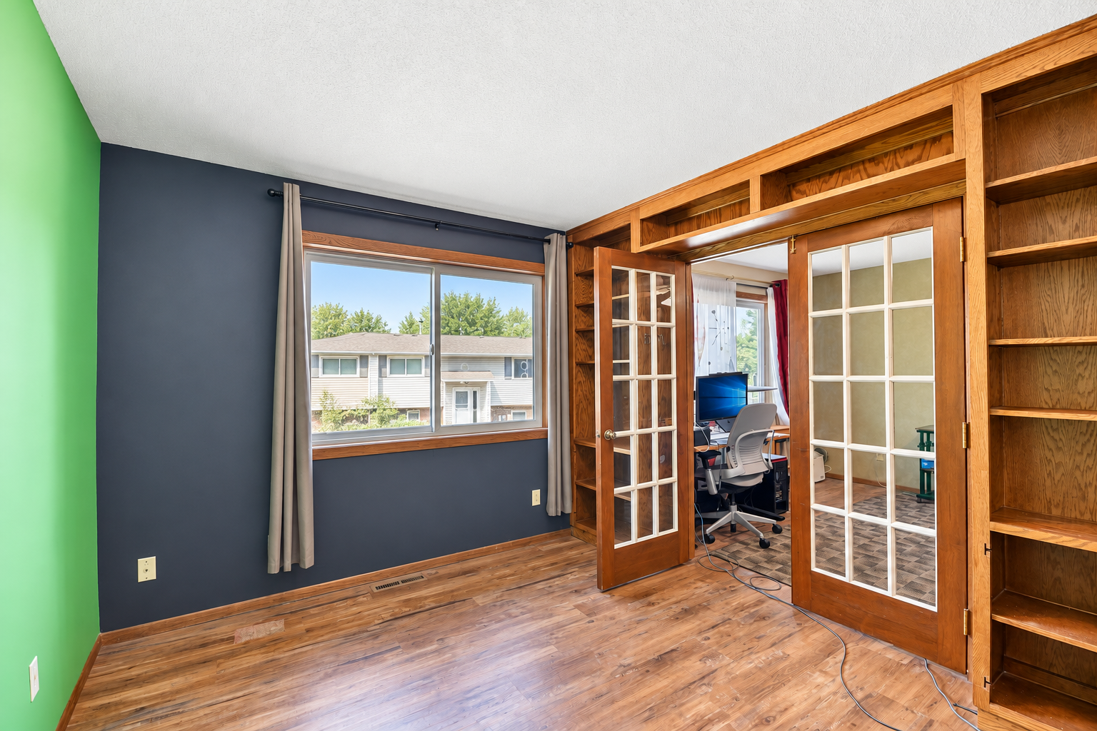 Interior room with hardwood floors and built-in shelves, opening through French doors to a home office.