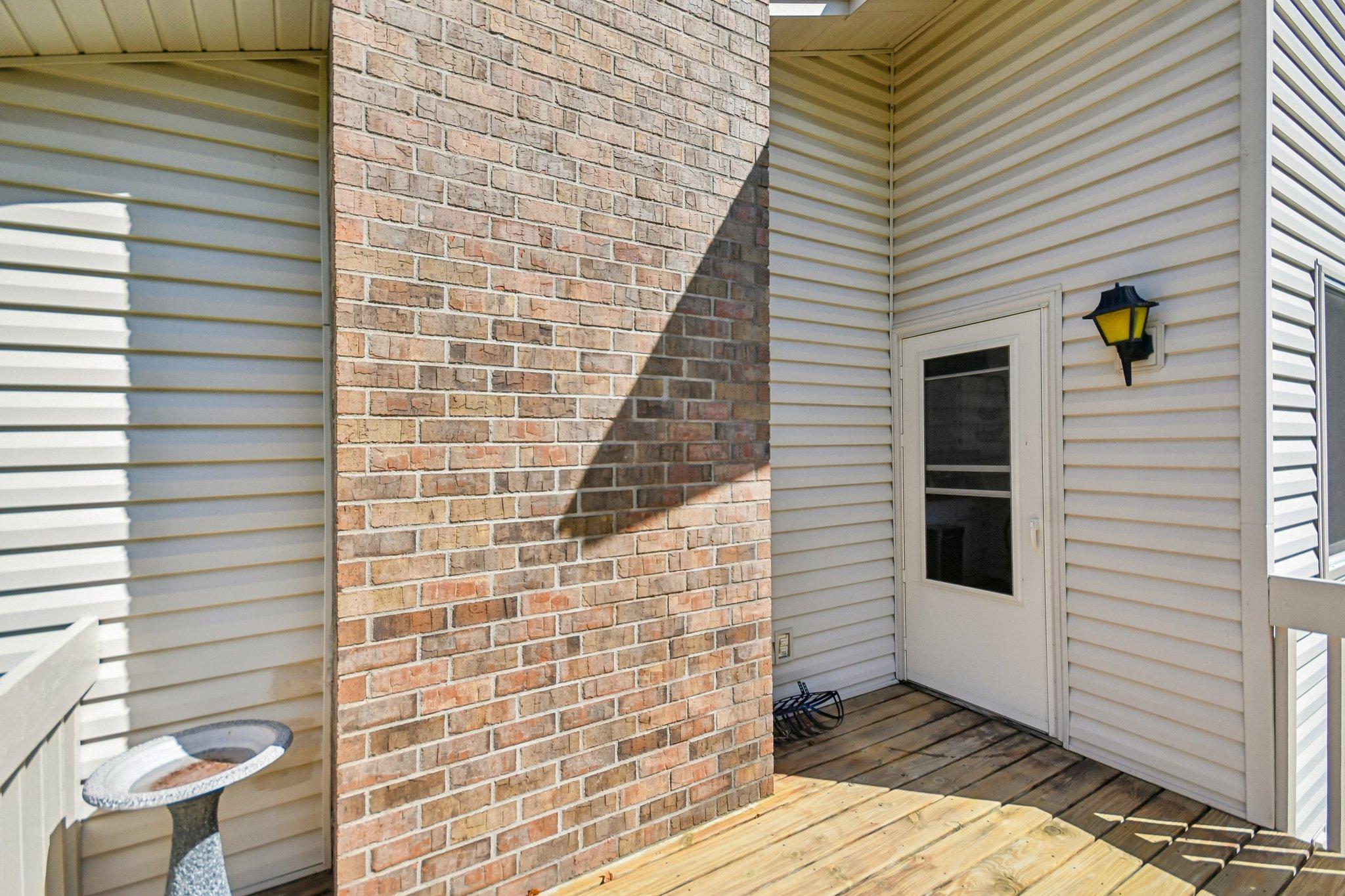 Exterior deck entry with a brick column, white screen door, and wall lantern.