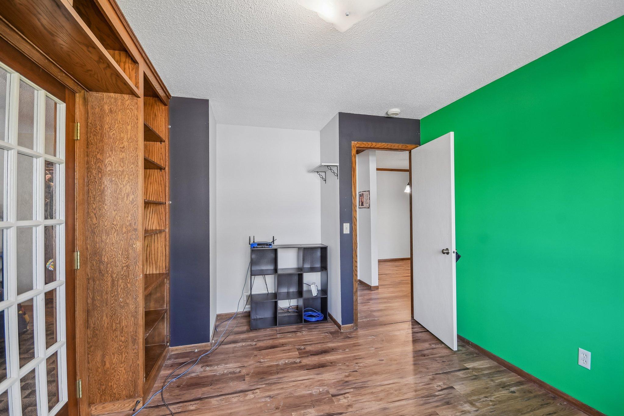 Interior room with built-in wooden shelving, a bright green accent wall, and an open doorway.