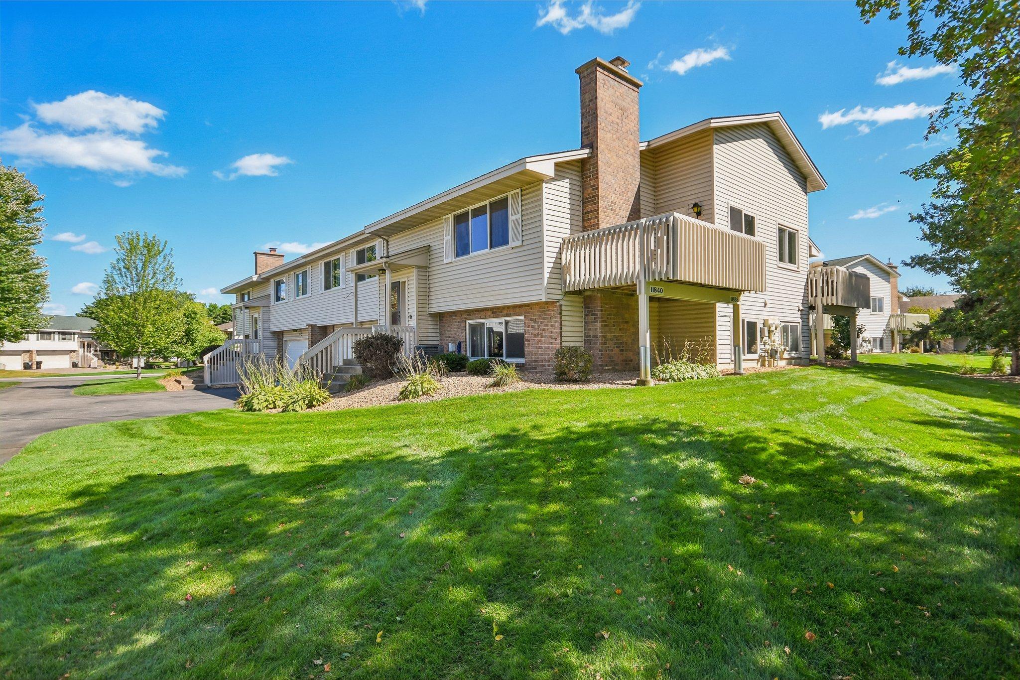 Light-sided residence with brick chimney and raised balcony above a broad green lawn.