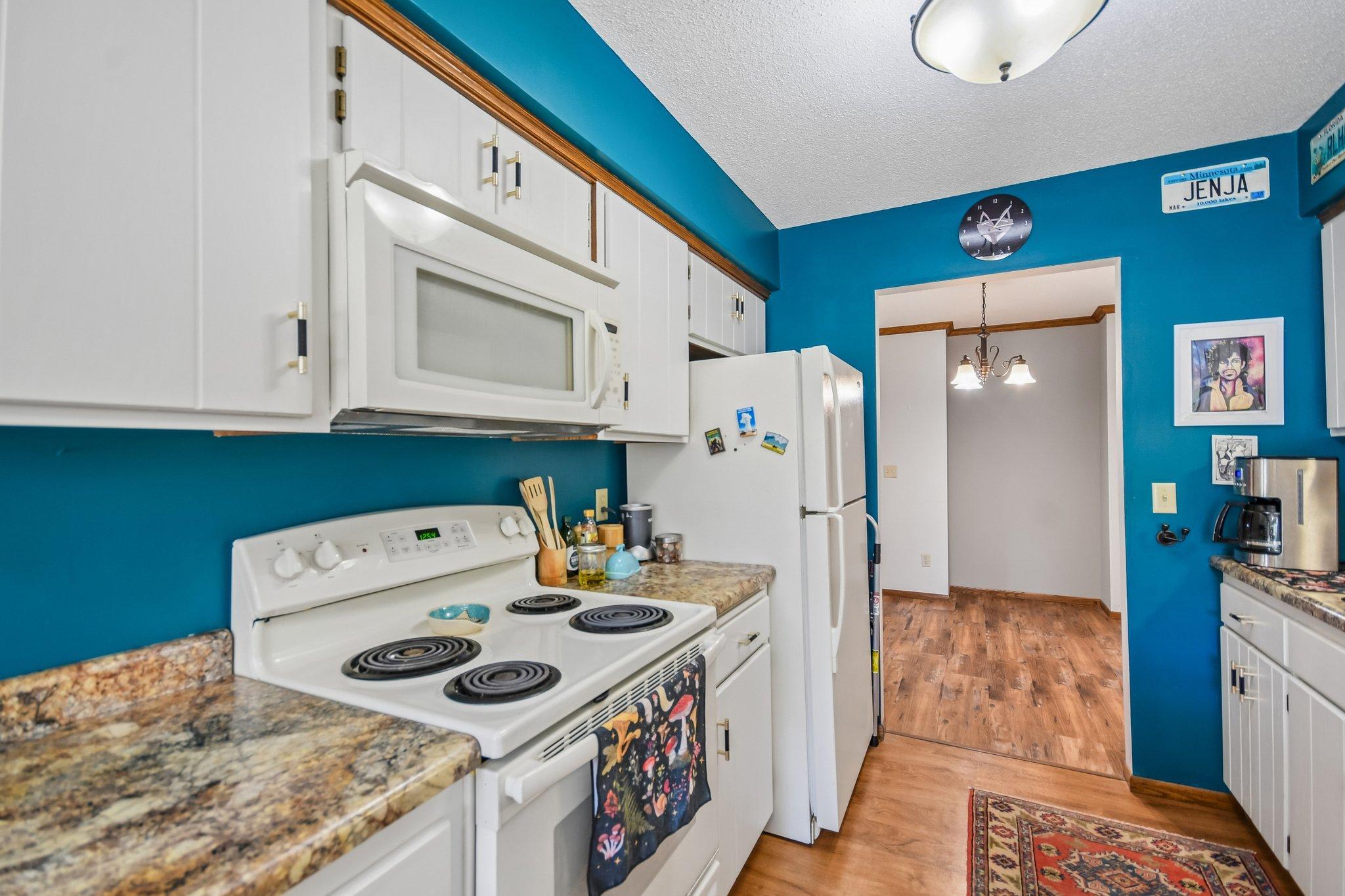 Kitchen with teal walls, white cabinets and appliances, speckled counters, and wood flooring.