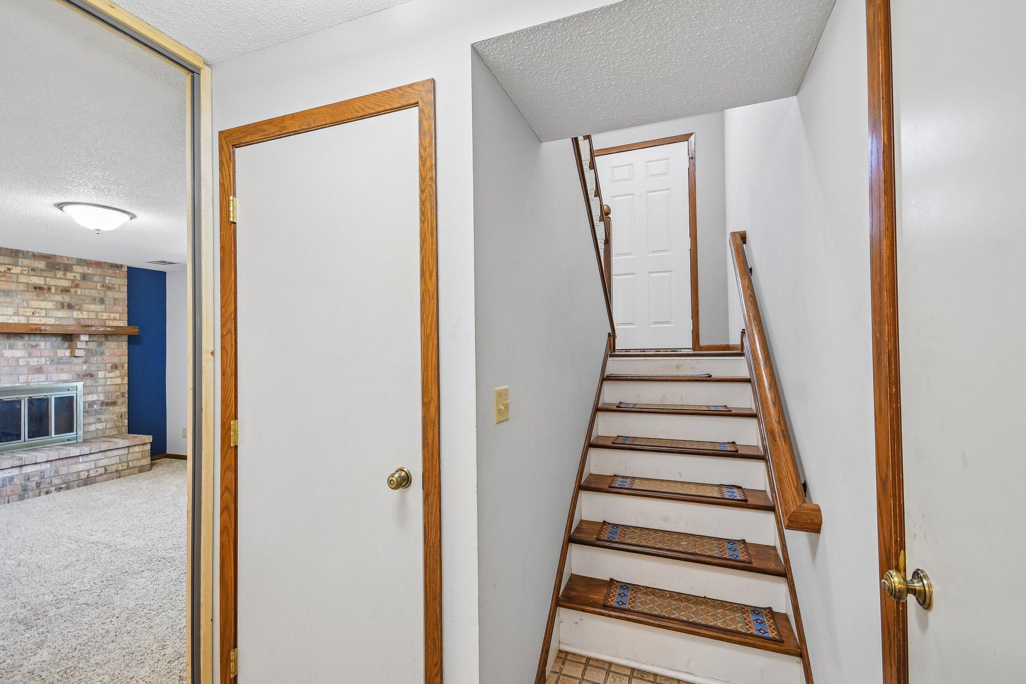 Interior staircase with wood railing and patterned runners, beside a glimpse of a brick fireplace.