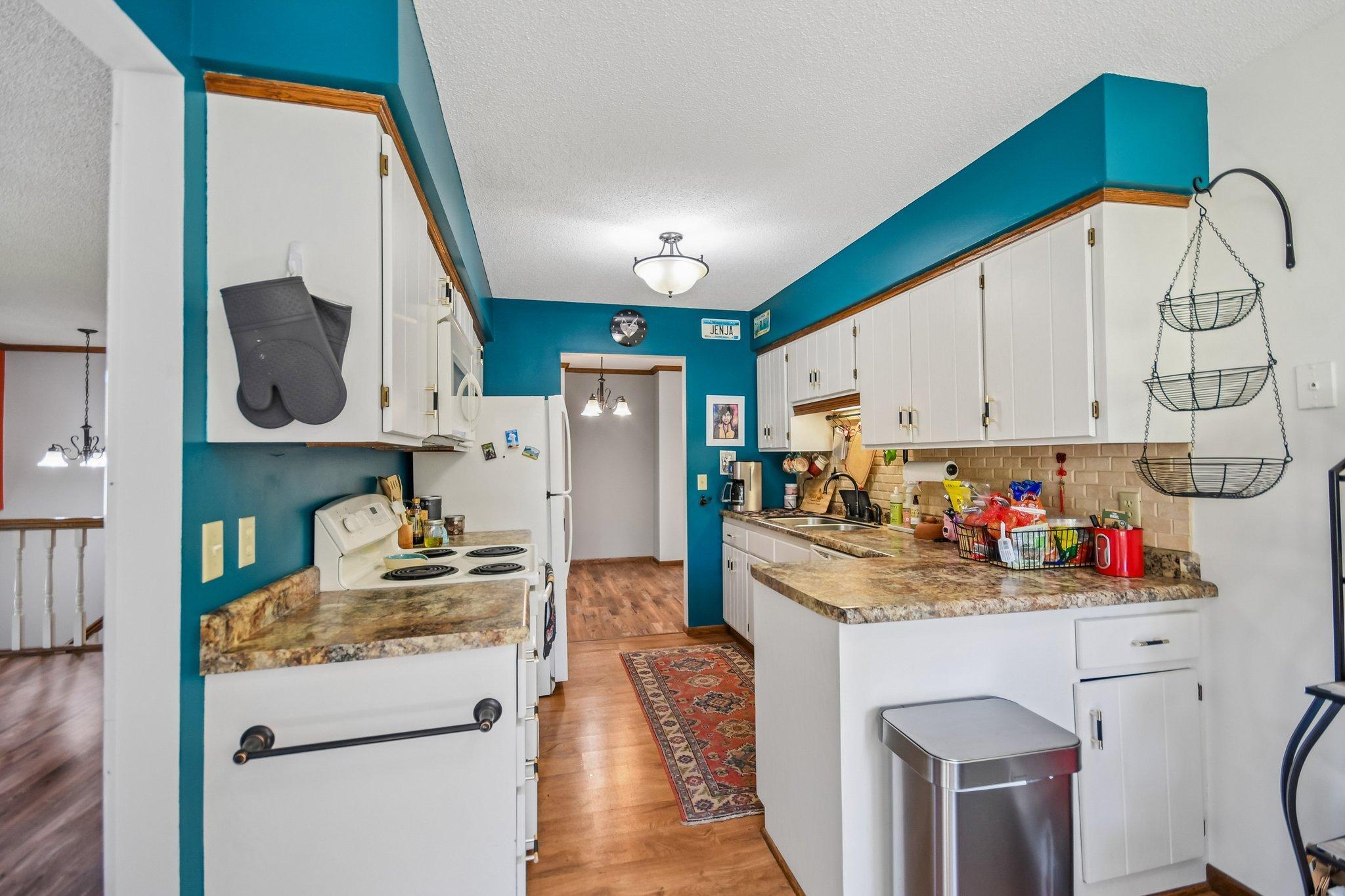 Kitchen with teal walls, white cabinets, and a stone-look peninsula countertop.