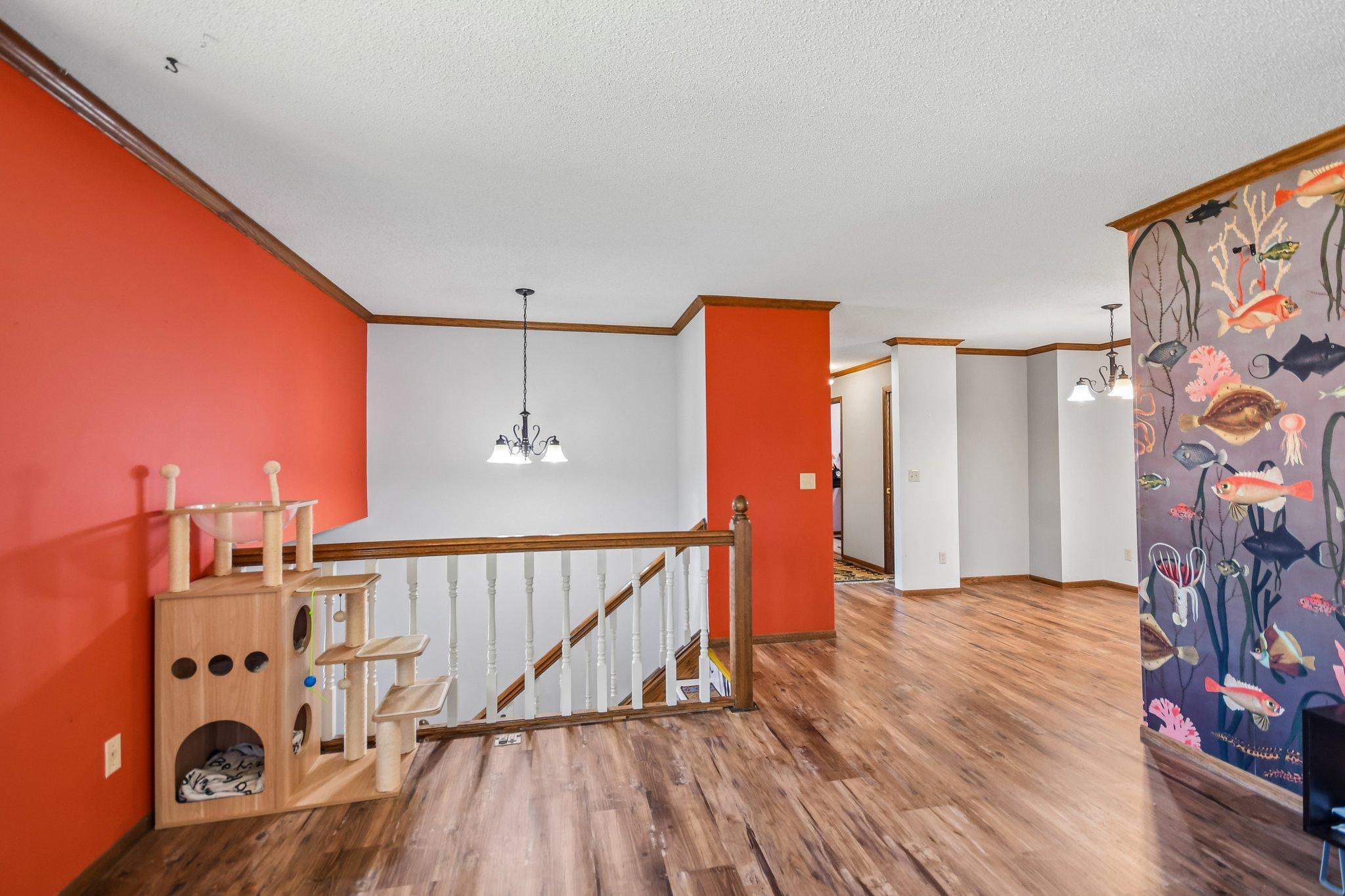 Upstairs landing with wood-look floors, red walls, a cat tree, and colorful fish wallpaper.