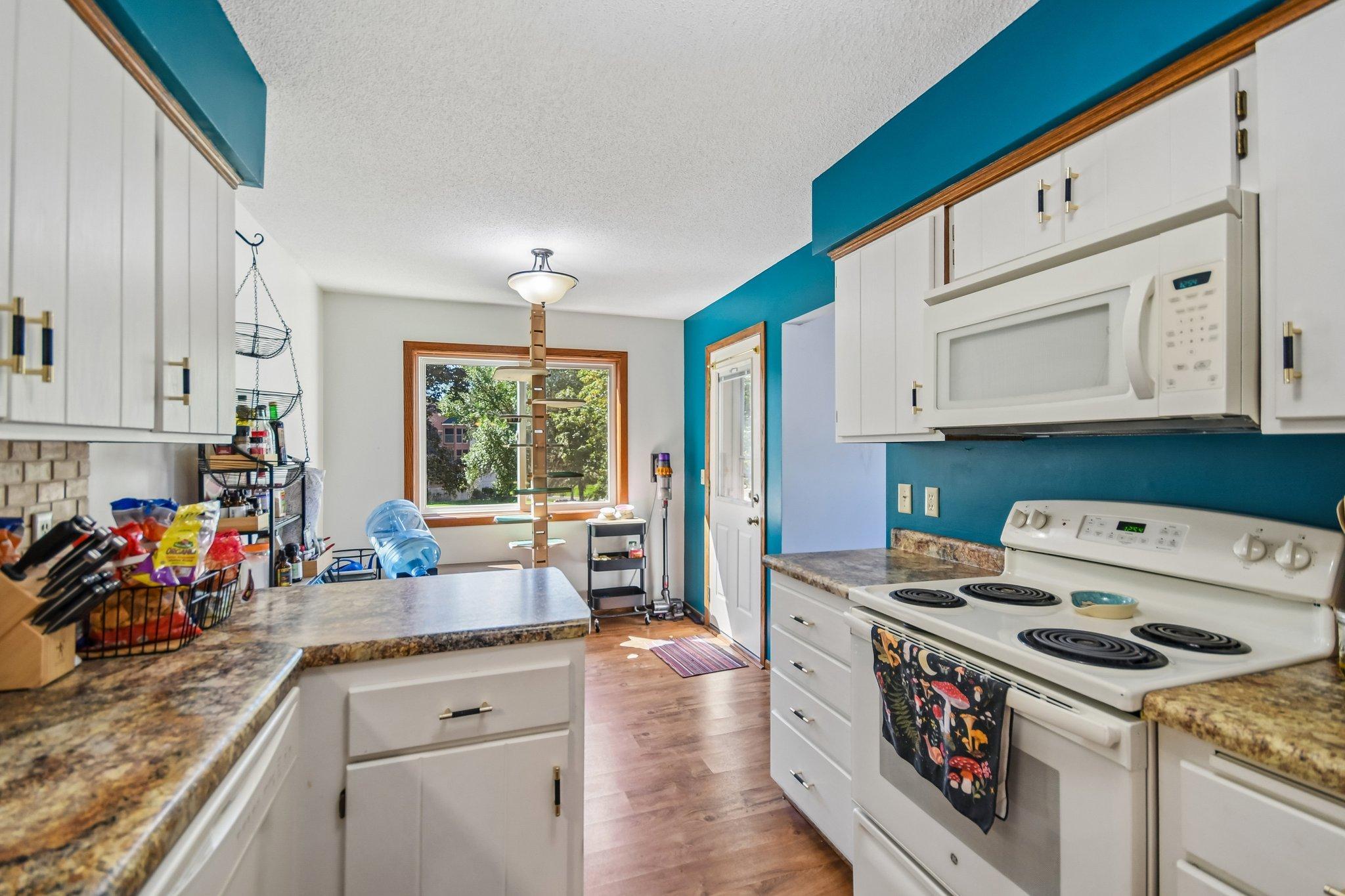 Kitchen with white cabinets and stone counters, teal walls, a small island, and a window overlooking leafy trees.