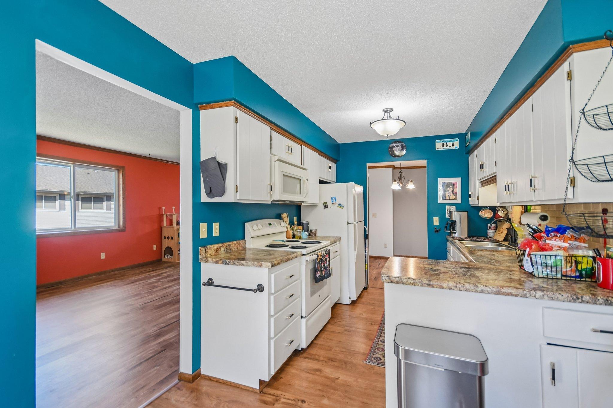 Kitchen with teal walls, white cabinets, stone-look counters, and an opening to a red-walled room.