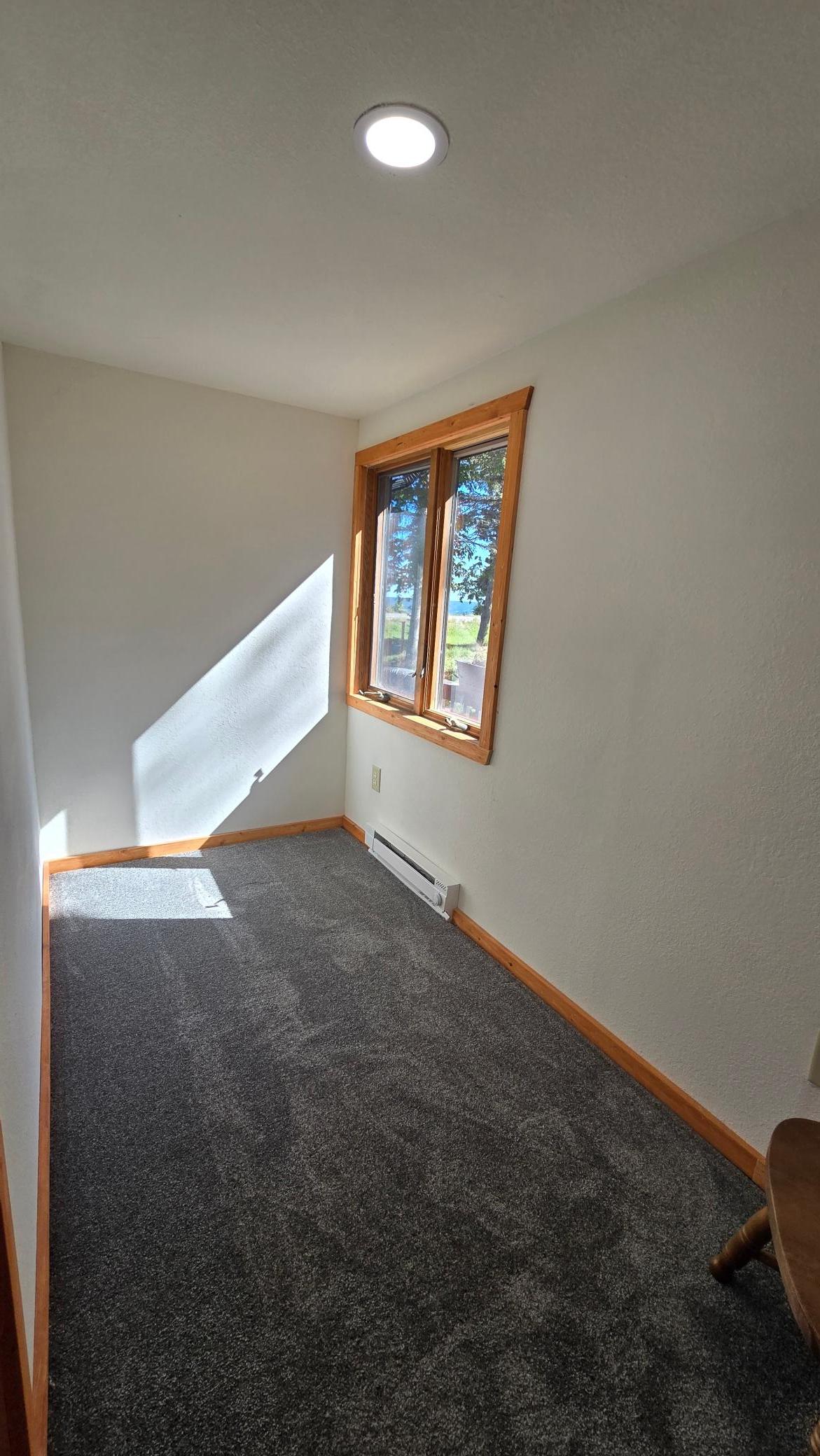 Small carpeted room with a wood-trimmed window, baseboard heater, and a glimpse of water outside.