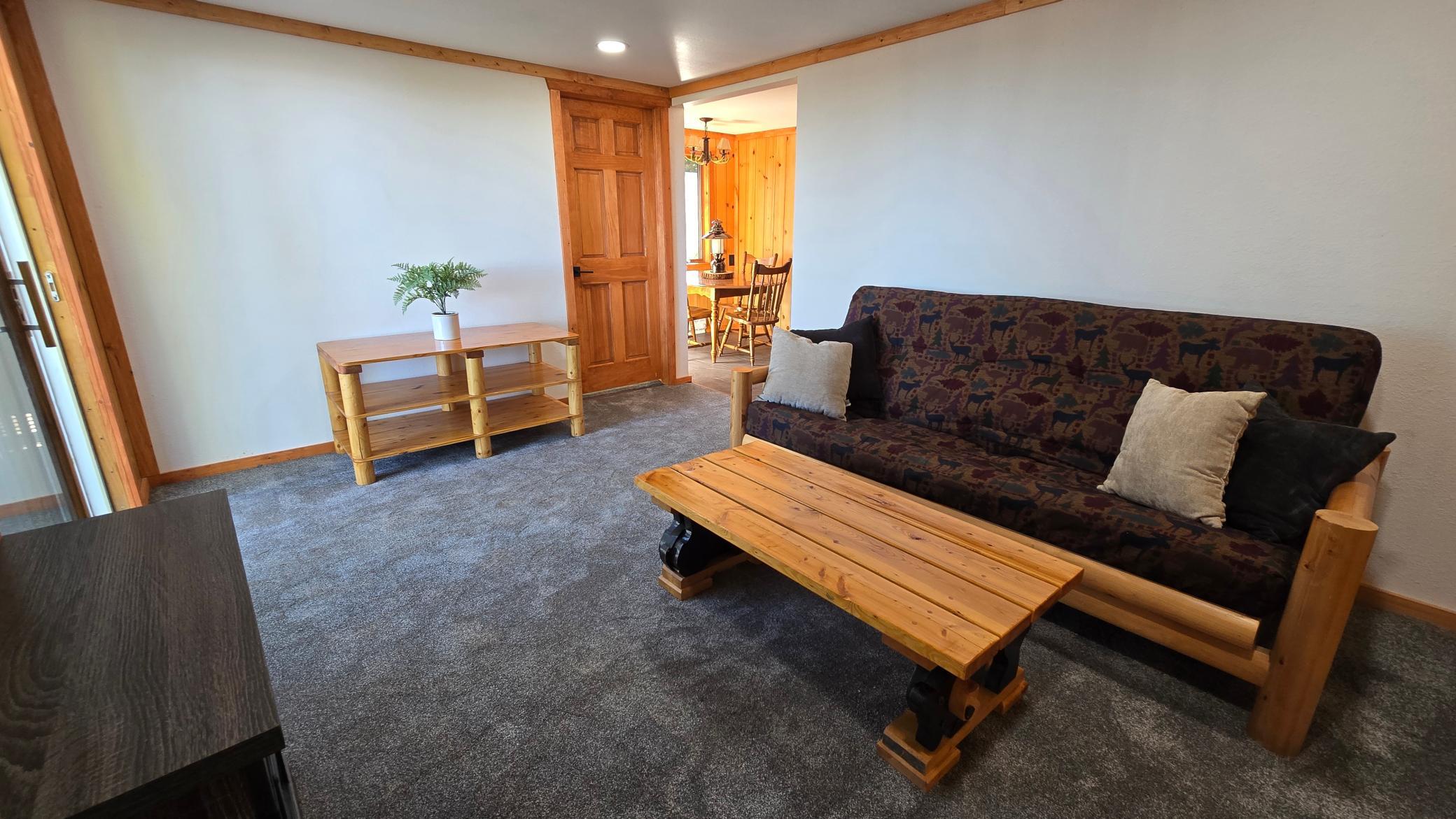 Living room with a patterned sofa, rustic wooden tables, gray carpet, and doorway to a dining area.