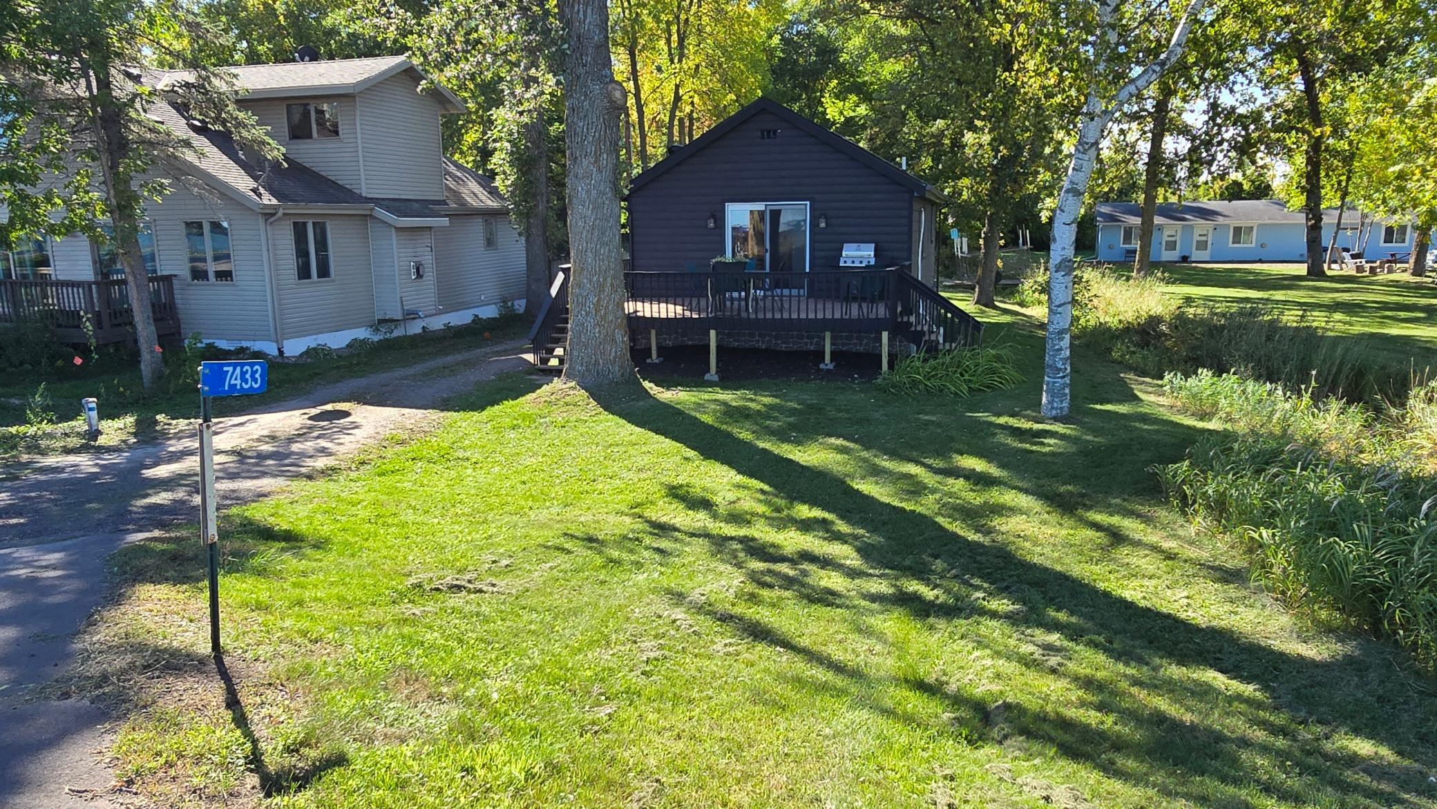 Property exterior with a raised deck, shaded grassy yard, and a post marked 7433.