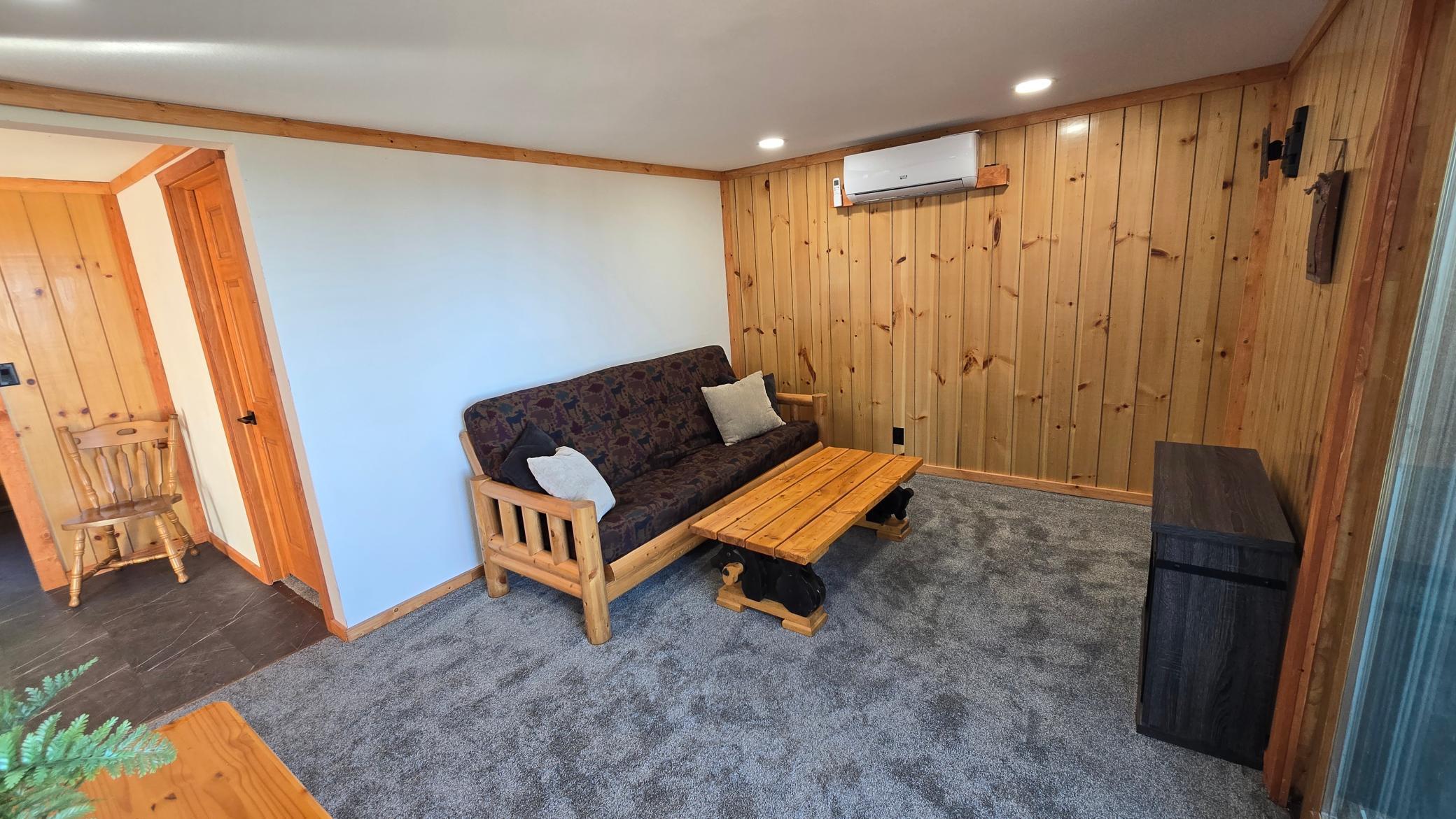 Living room with a futon and wooden coffee table against a wood-paneled wall.
