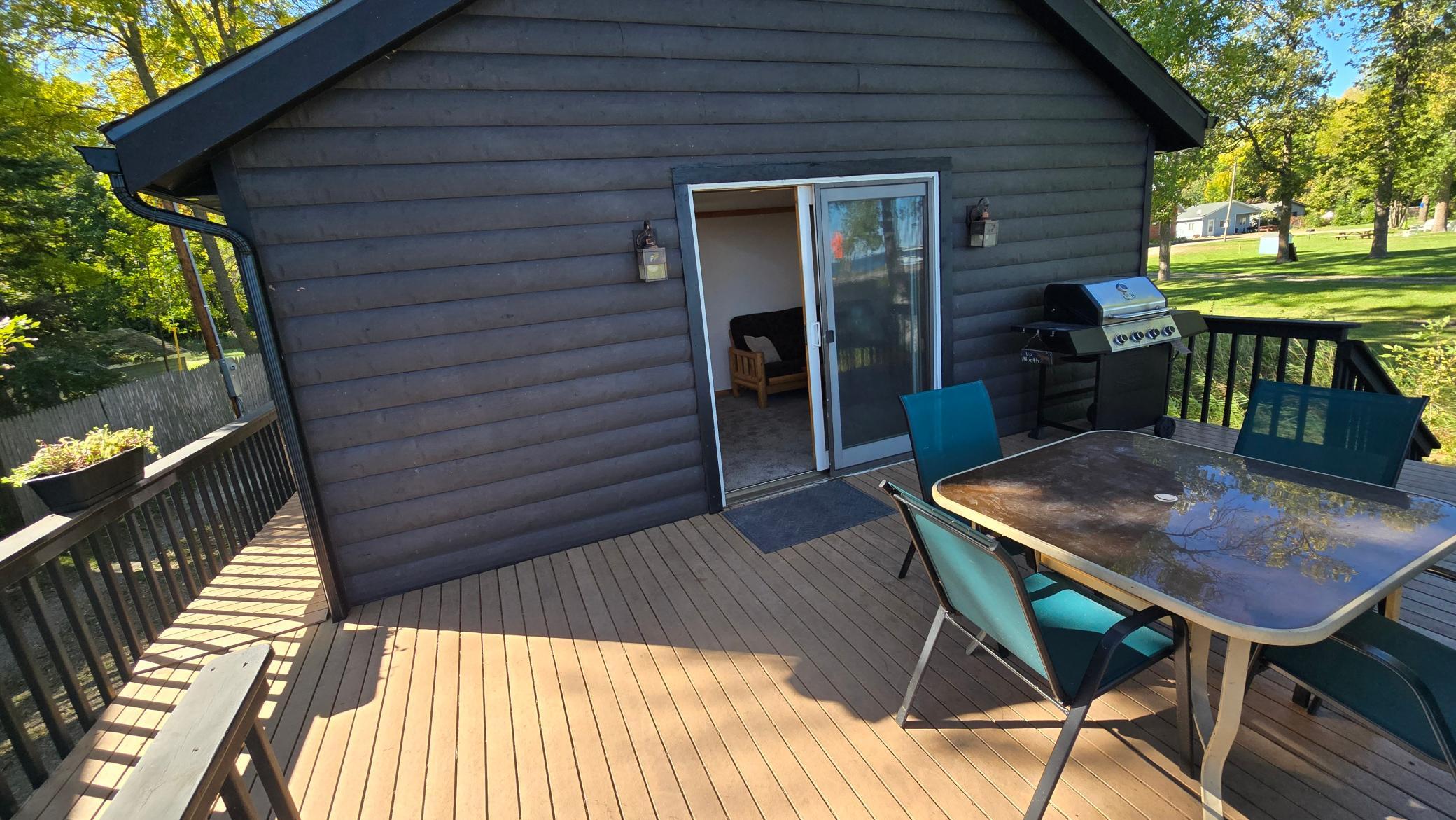 Wooden deck with patio table, turquoise chairs, and gas grill beside a dark-sided home.