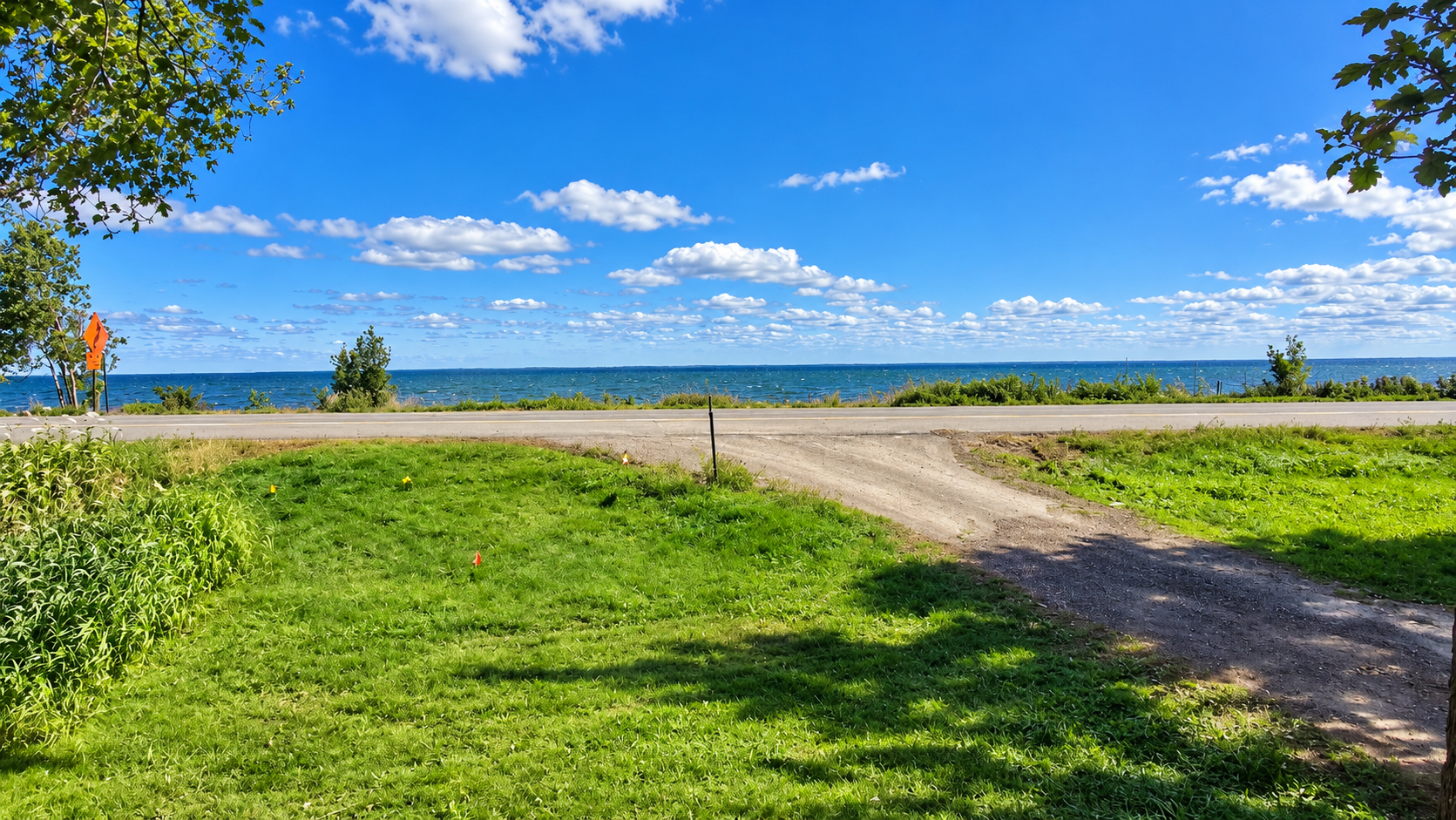 Grassy vacant lot with a dirt driveway, road, and lakefront view.