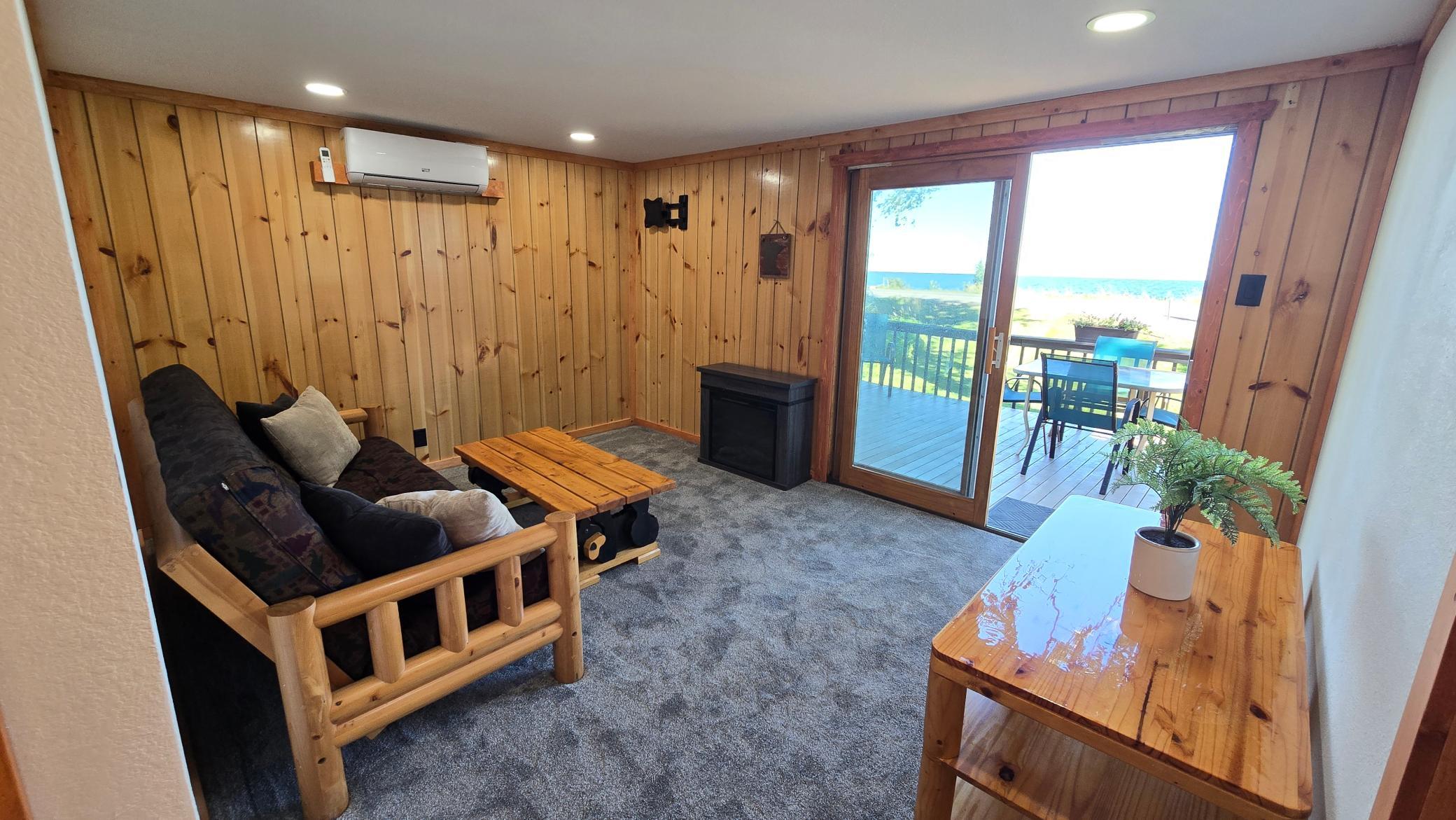 Wood-paneled living room with a rustic sofa and sliding doors opening to a deck overlooking the lake.