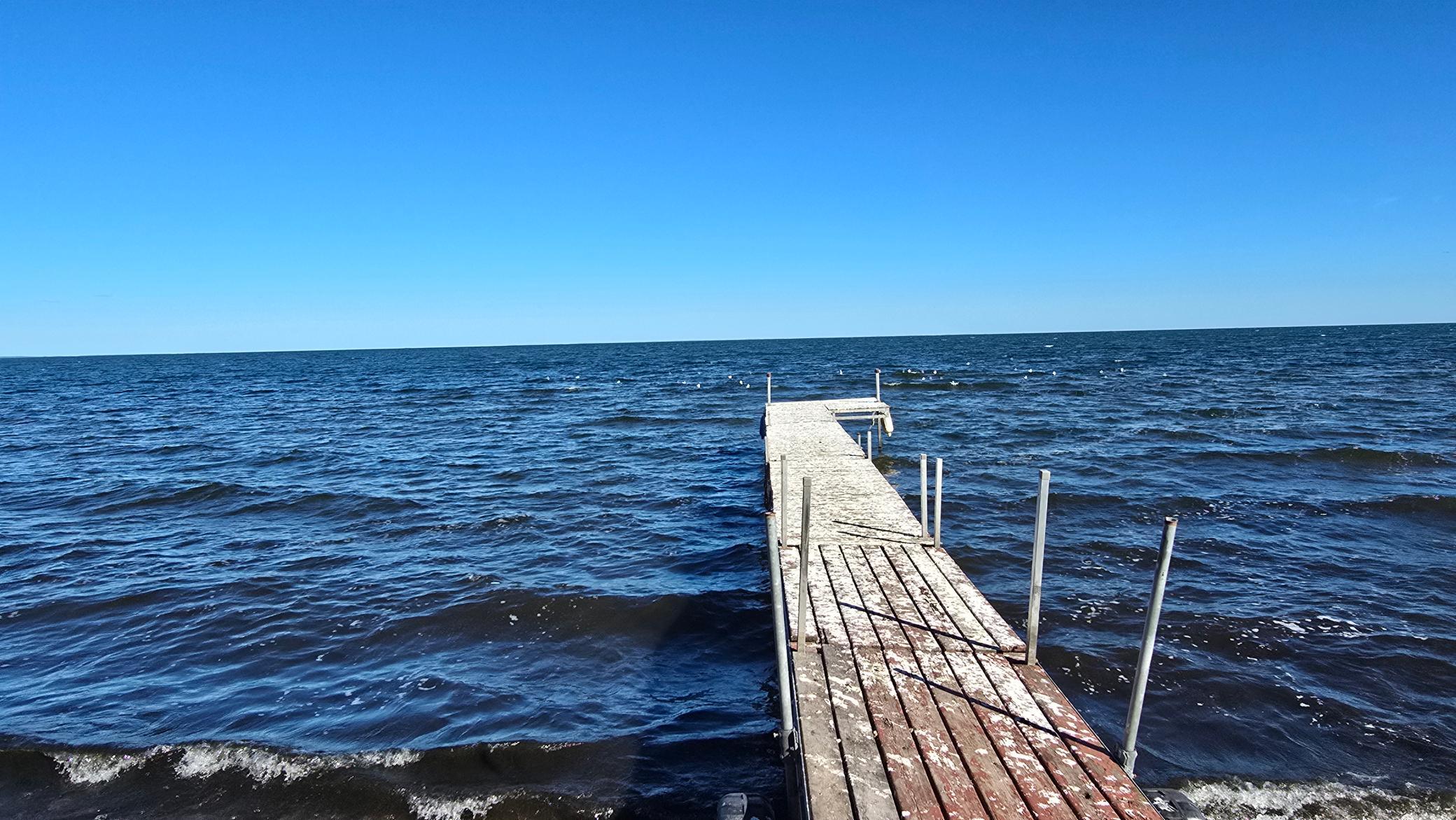 Wooden dock extending into a choppy lake beneath a clear blue sky.