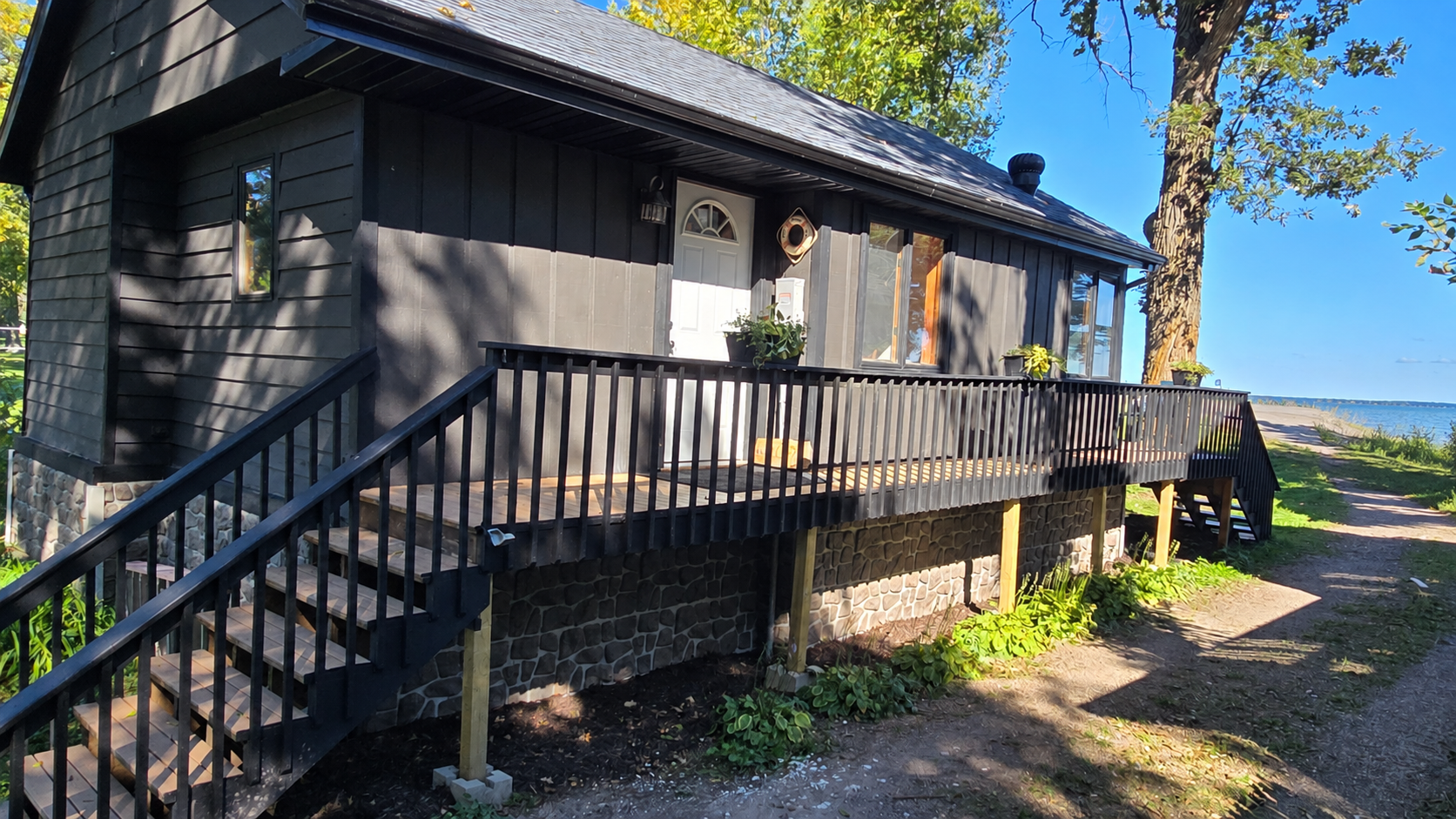 Dark-sided lakeside home with a long raised deck and stairs beside the water.