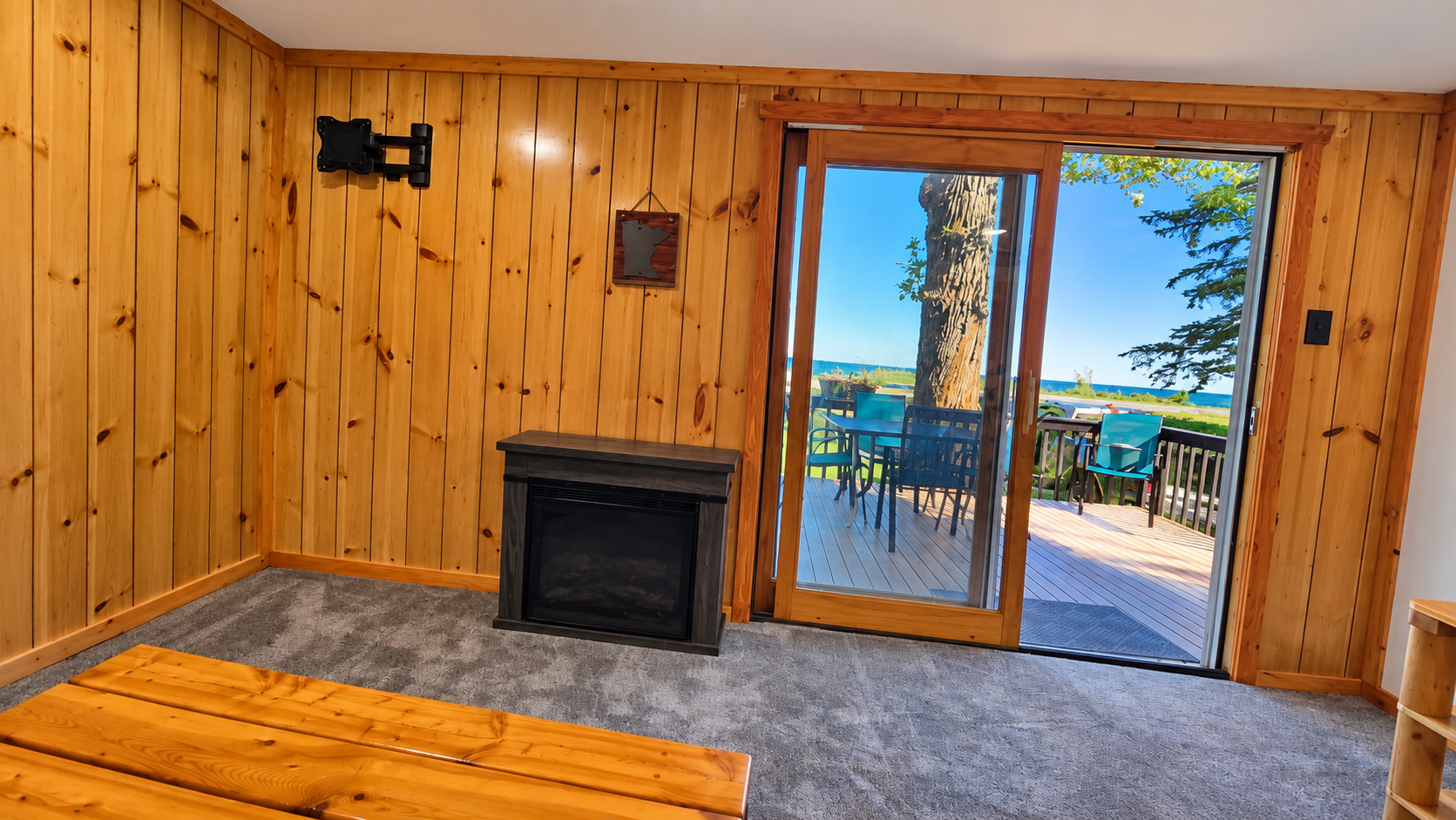 Pine-paneled room with a fireplace and sliding door opening onto a lake-view deck.