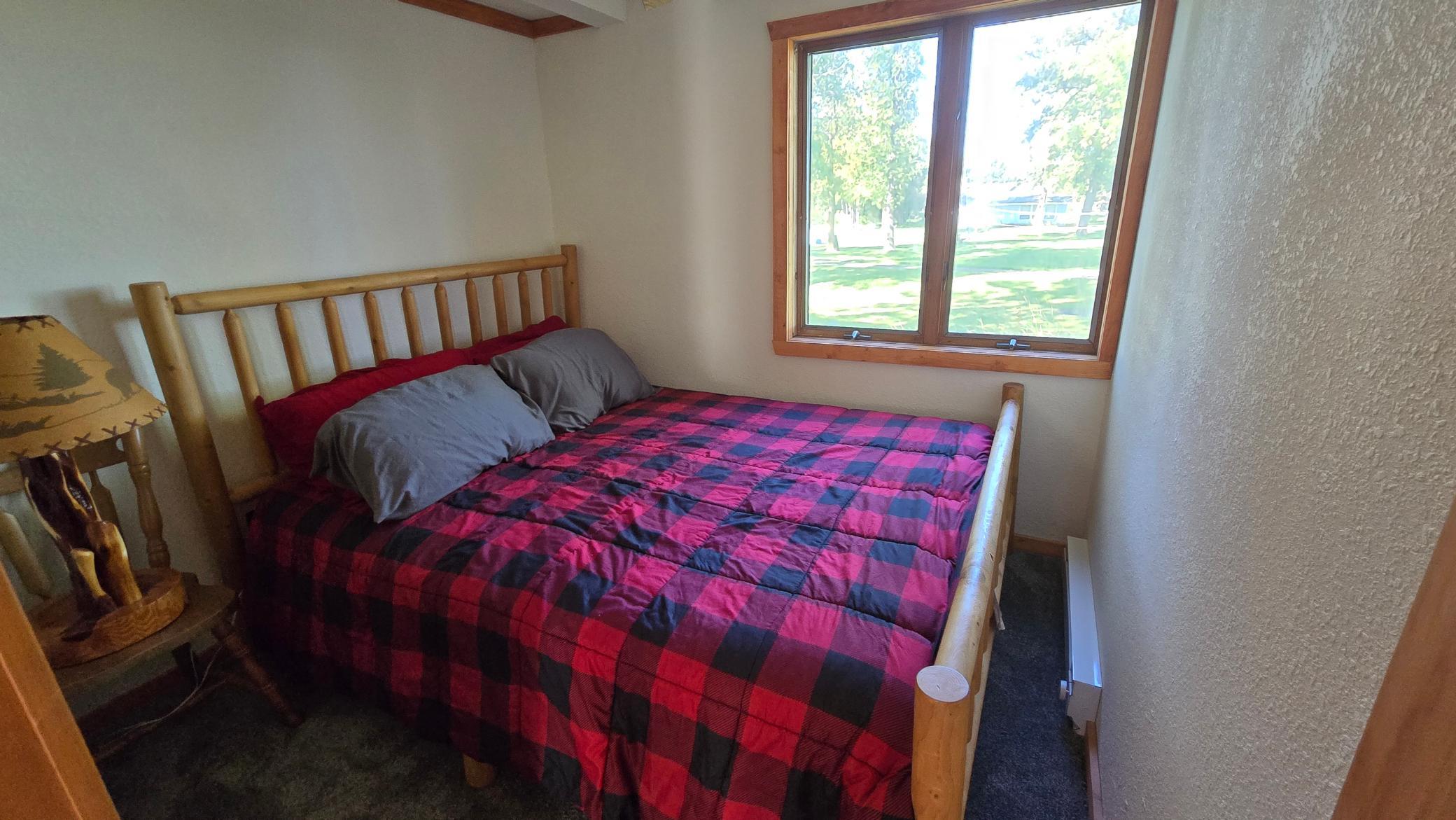 Bedroom with a log-style bed covered in a red and black plaid quilt beside a large window.