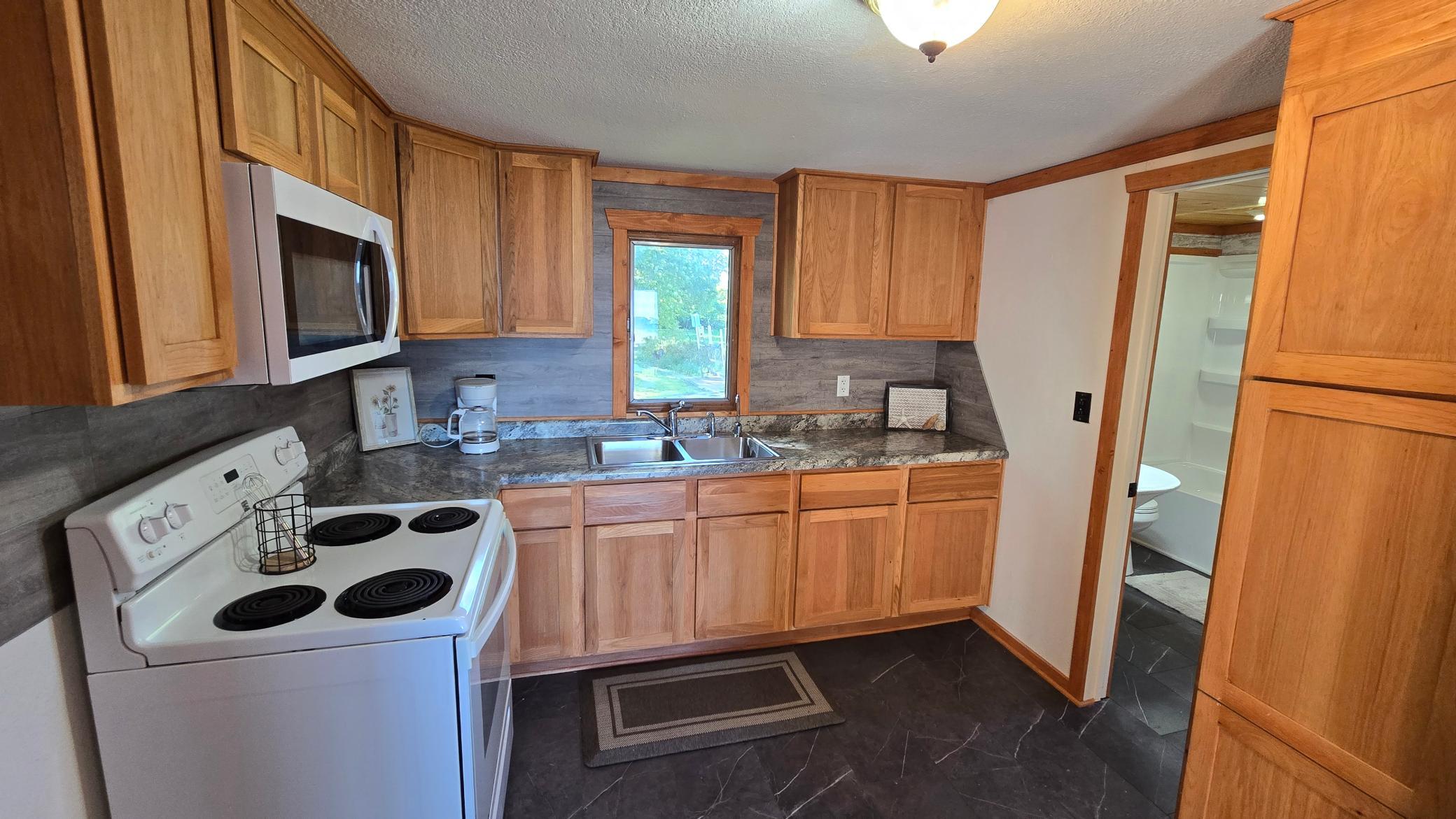 Kitchen with wood cabinets, dark countertops, and a sink beneath a window.