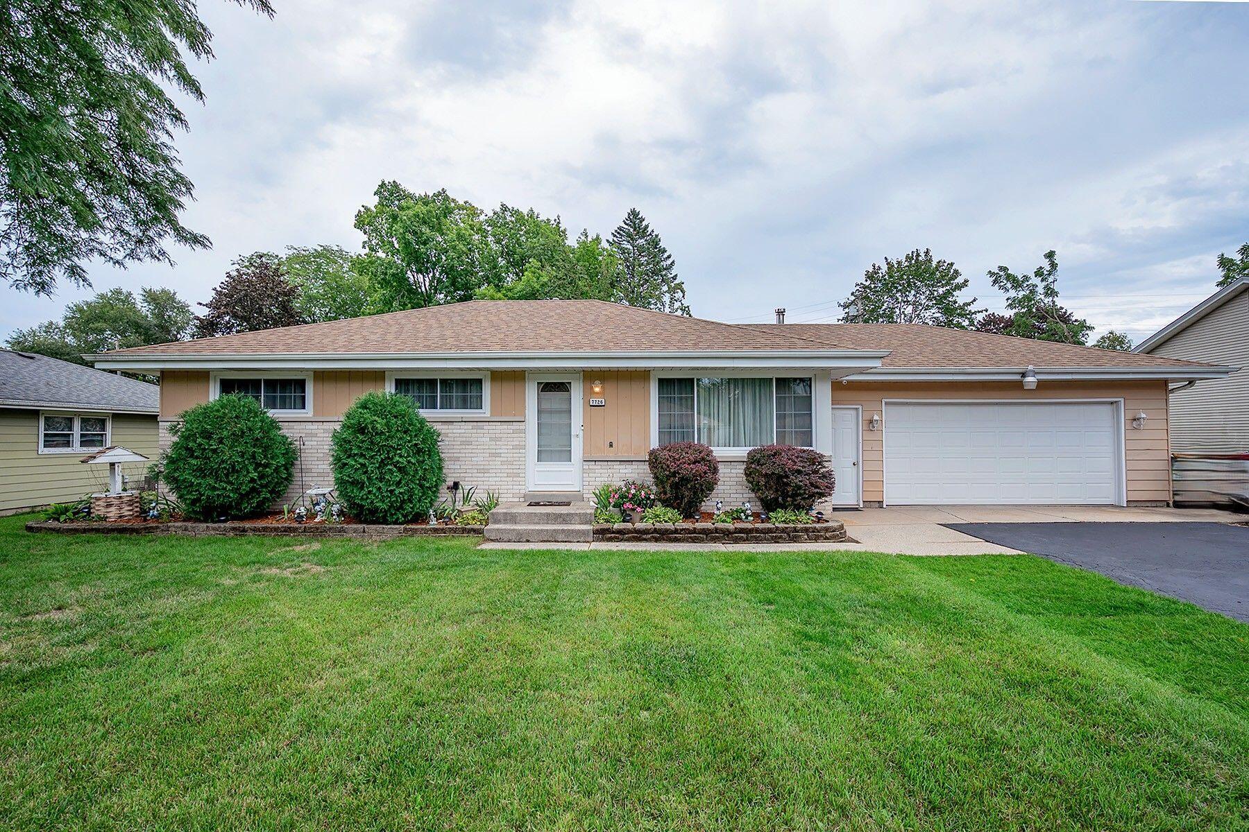Single-story tan ranch house with a brick facade, two-car garage, and landscaped front lawn.