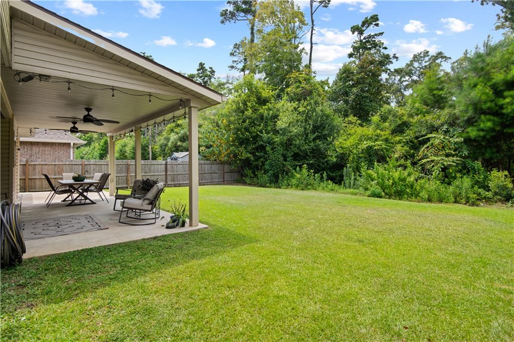 Fenced backyard with a covered, furnished patio overlooking a broad lawn and tree line.