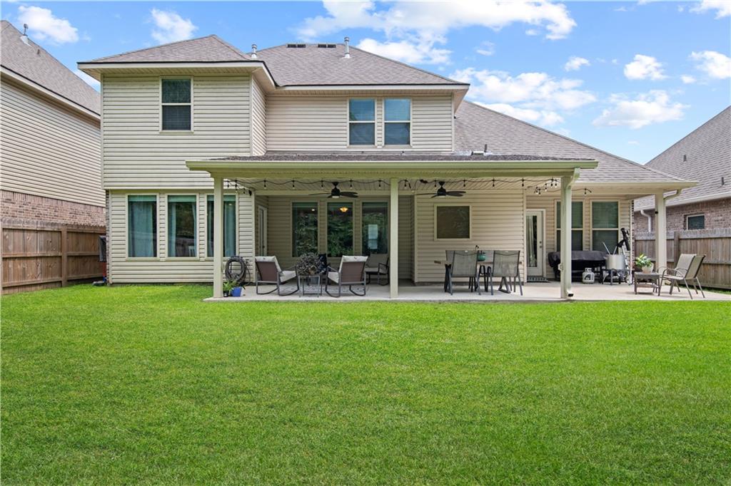 Two-story house with a covered, furnished patio and broad green lawn.