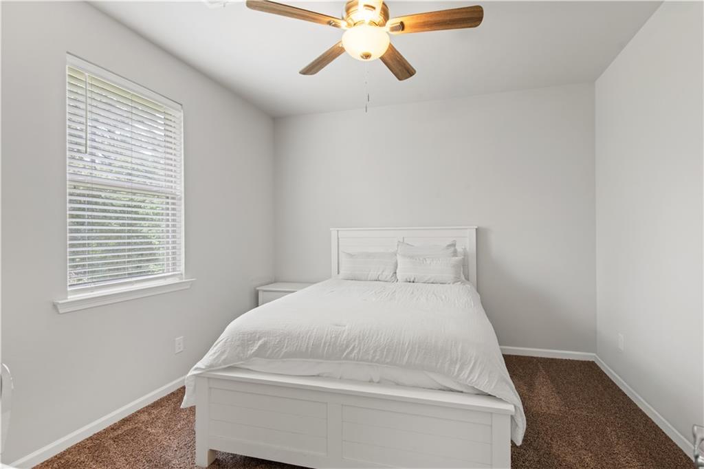Furnished bedroom with a white bed, window blinds, ceiling fan, and brown carpet.