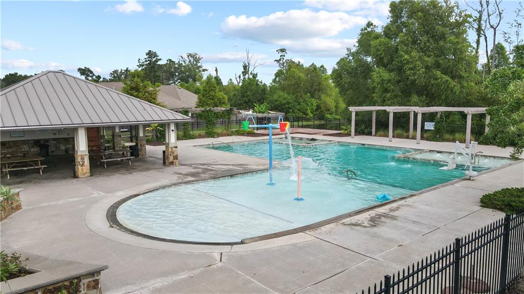 Outdoor pool with a shallow splash area, shaded pavilion, and fenced deck.